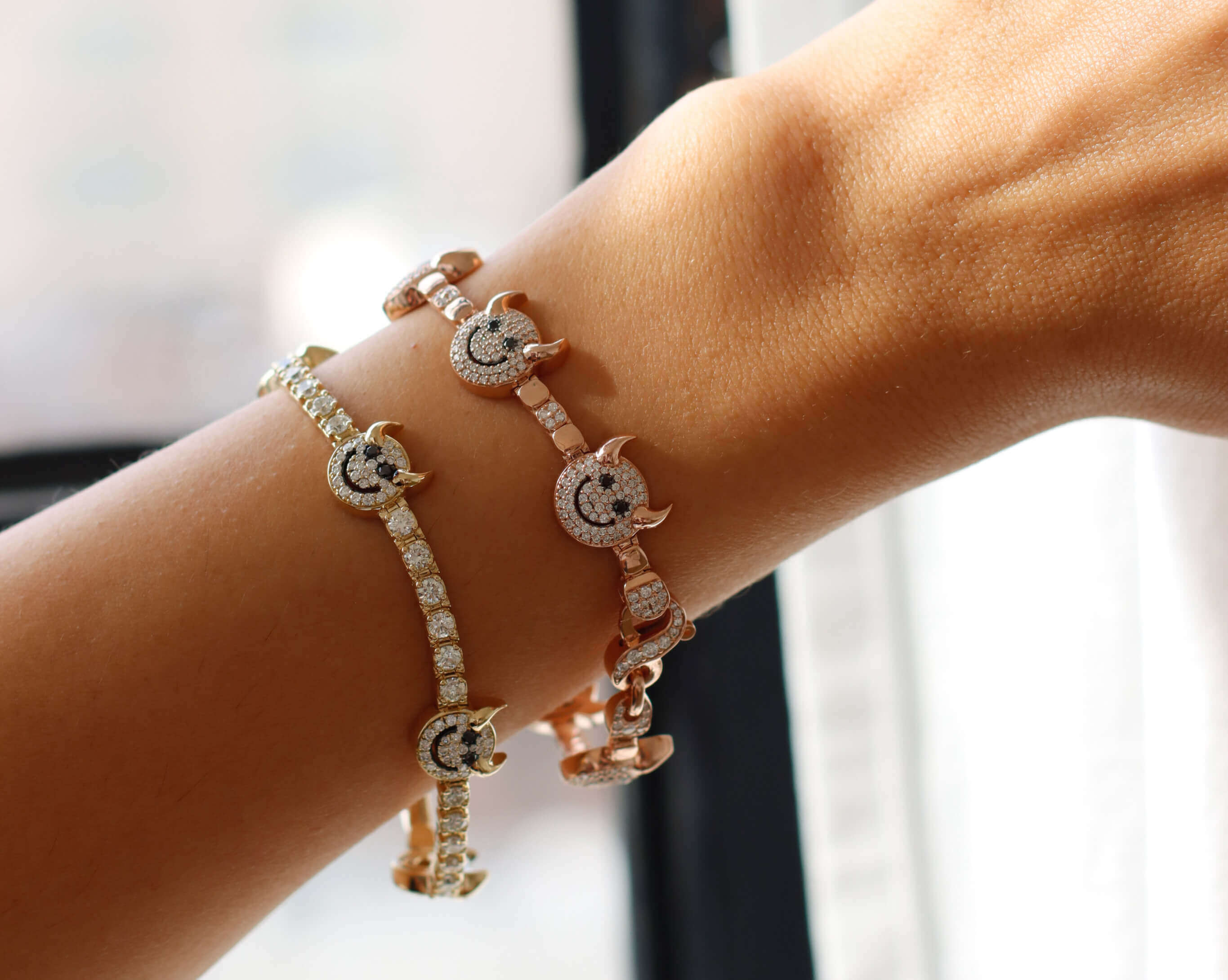 A persons arm is adorned with two sparkly bracelets, one silver and one rose gold, featuring crescent moon and star designs encrusted with small gems, against a softly lit background.
