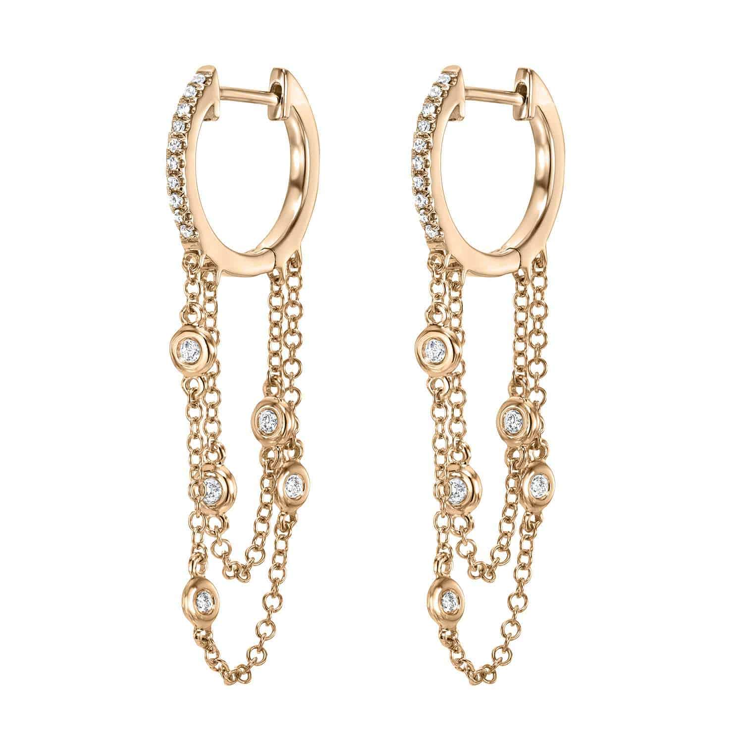 The Diamond Waterfall Huggies by Janet Heller Fine Jewelry feature gold hoops with rows of small, round white gemstones and three hanging chains adorned with spaced gemstones, creating an elegant cascading design.