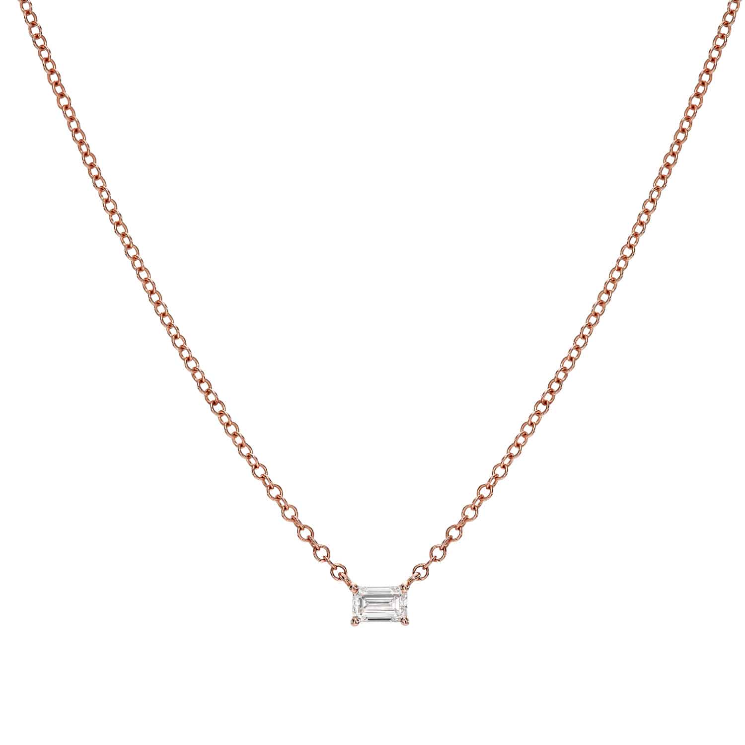 The Solitaire Emerald Cut Diamond Necklace by Janet Heller Fine Jewelry features a thin rose gold chain with a central small rectangular diamond pendant. Delicate loops enhance its elegance, offering a luminous presence against a white background.