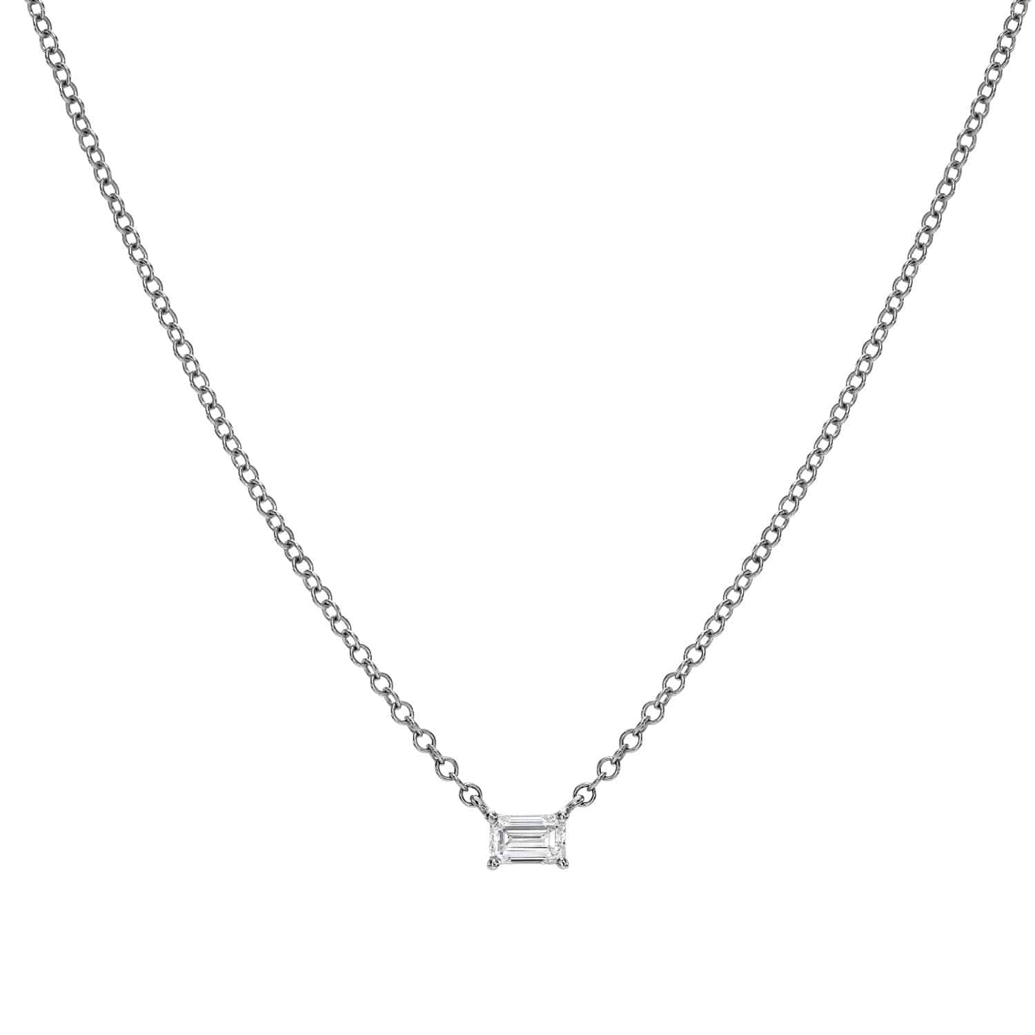 The Solitaire Emerald Cut Diamond Necklace by Janet Heller Fine Jewelry showcases a small rectangular-cut diamond pendant on a fine chain. Set against a plain white background, it exudes understated elegance.