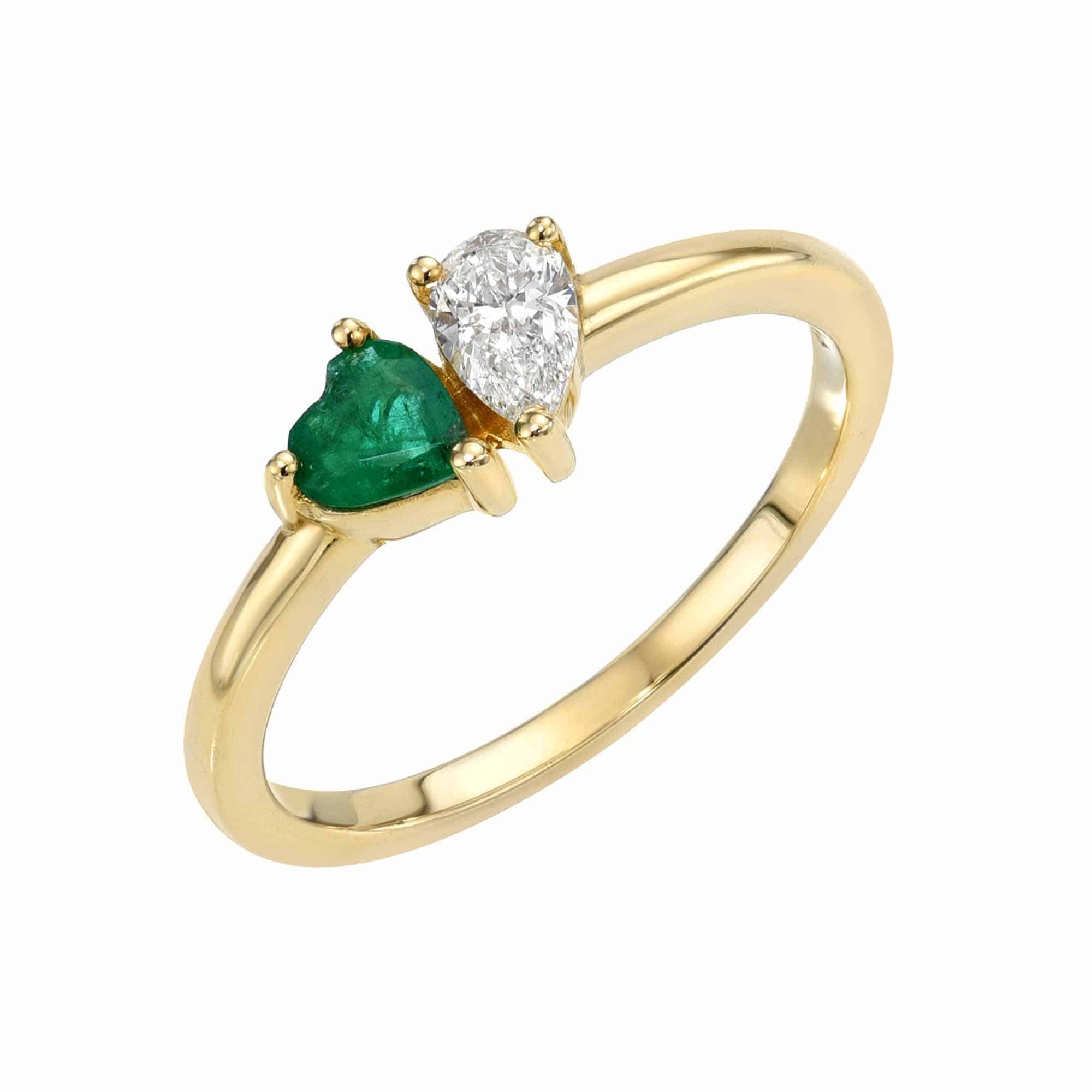 The Emerald & Diamond Toi et Moi Ring by Janet Heller features a heart-shaped green emerald and a pear-shaped white diamond set side by side on a simple gold band, highlighting fine jewelry design.