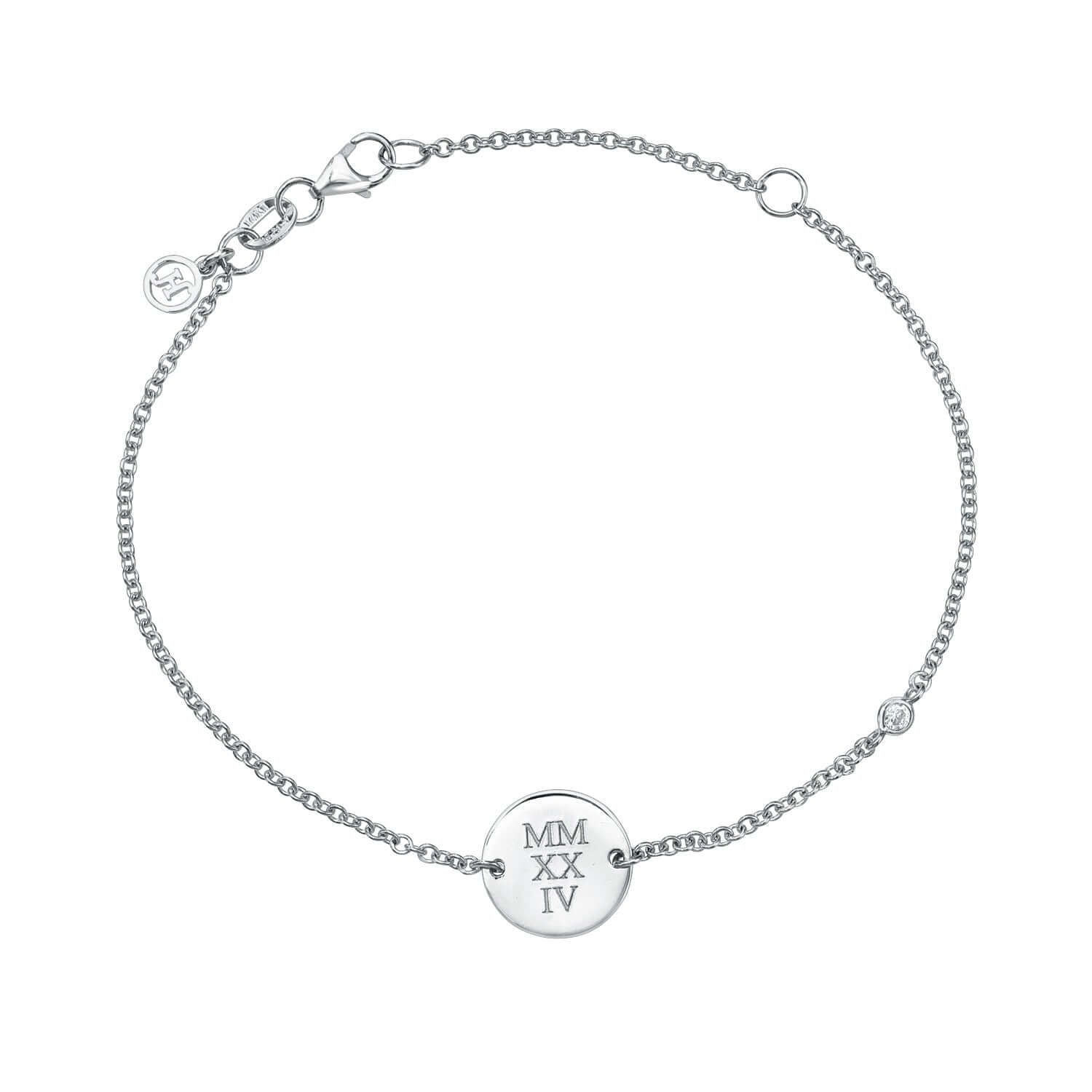 The Mini Diamond Sketch Bracelet is a silver chain piece with a round charm engraved with MMXXIV. It includes an adjustable clasp and a small circular tag near the clasp.