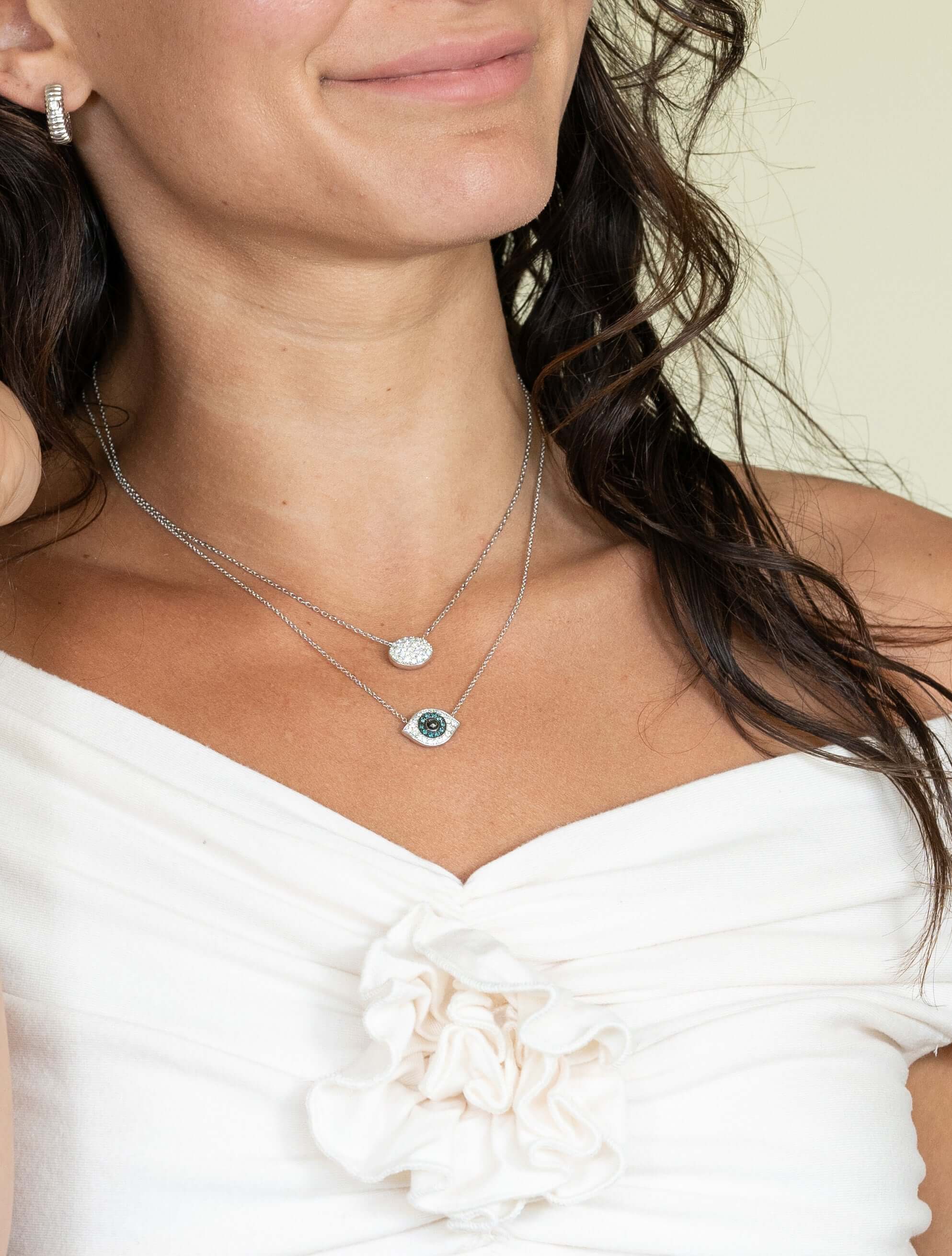 Wearing a white off-the-shoulder top with floral detail, she adorns herself with elegant janetheller fine jewelry. Her long, wavy hair beautifully complements the Blue & Black Diamond Evil Eye Necklace that shimmers as if customized just for her.