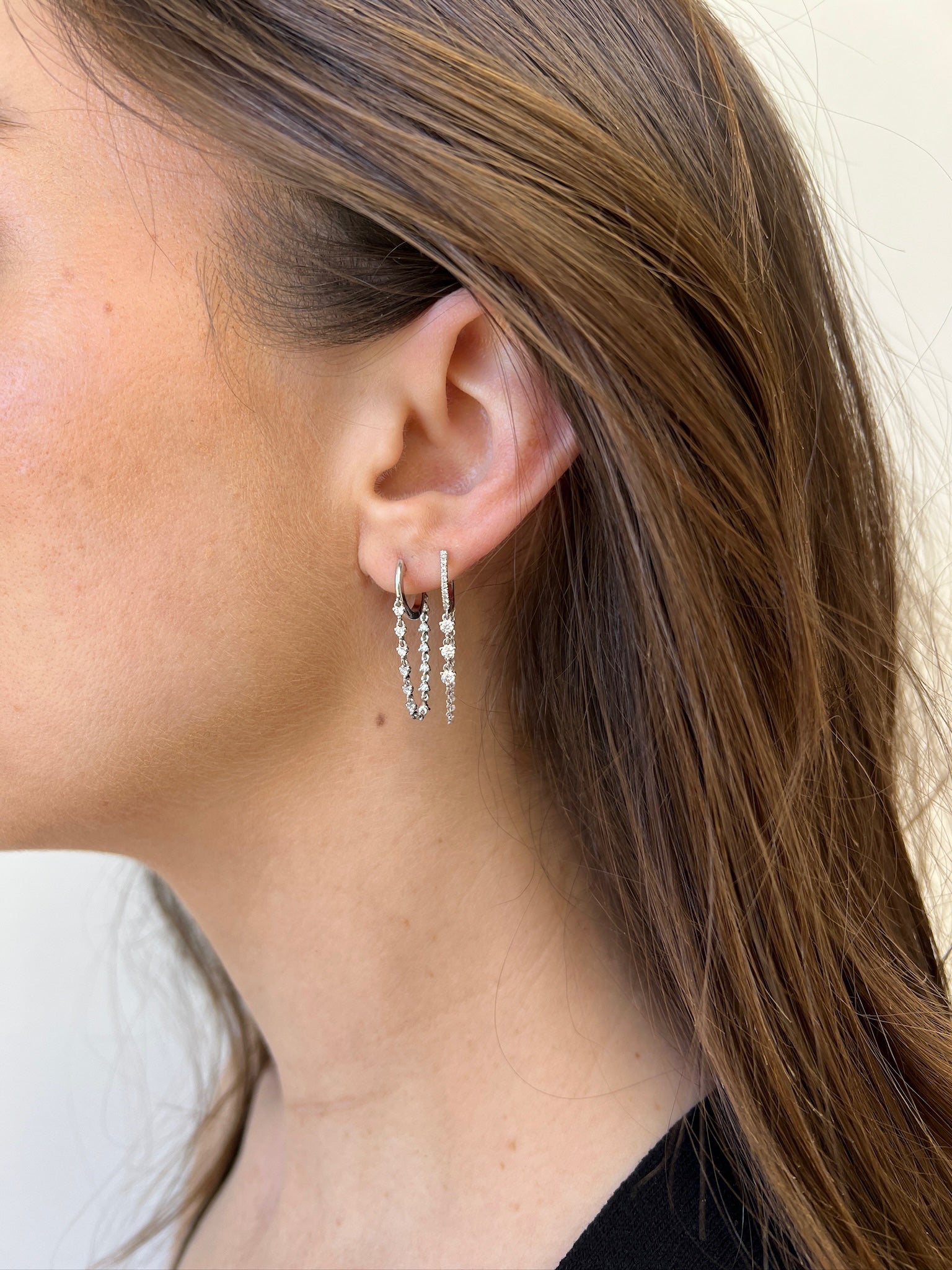The Diamond Cascade Drop Huggies from Janet Heller Fine Jewelry are crafted in 14KT gold. The dangling hoop earrings feature evenly spaced round diamonds connected by a delicate chain. The earrings can be worn alone or layered along the ear with other earrings.