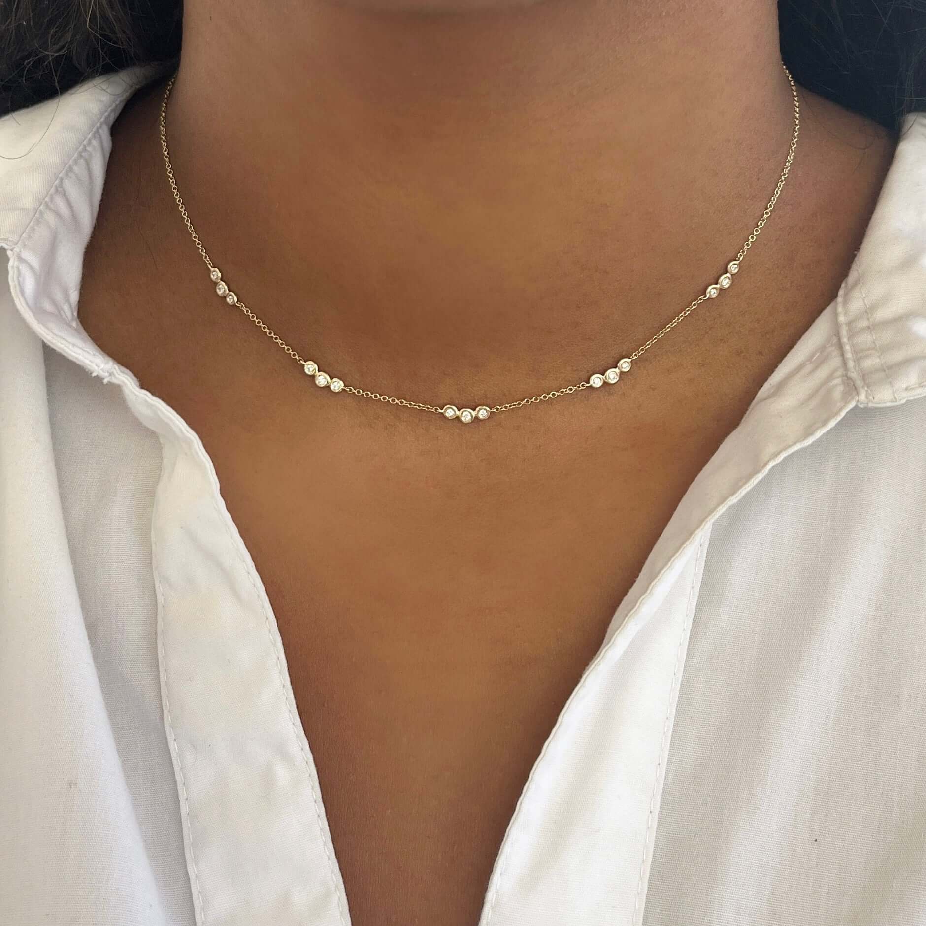The Bezel Diamond Trio Station Necklace by Janet Heller Fine Jewelry is crafted in 14KT gold.  It features a gold chain with clusters of three small, round diamonds set in circular bezels linked by delicate chains.  The necklace can be worn alone or layered with other necklaces.