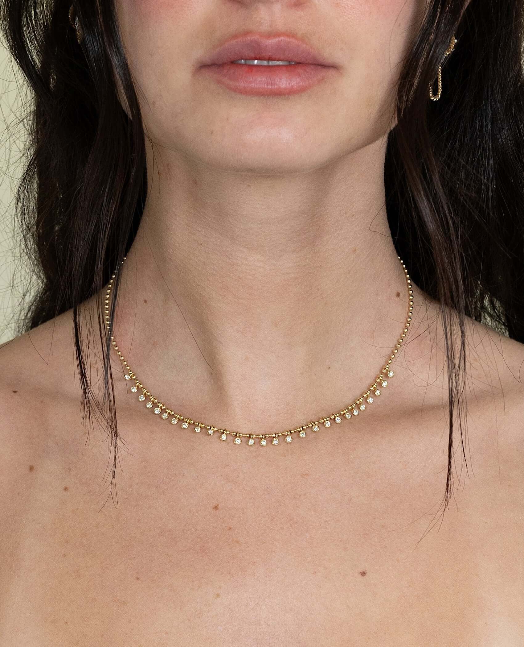 The Diamond Eisley Necklace from Janet Heller Fine Jewelry is crafted in 14KT gold. It features a chain of gold beads with dangling round diamonds. The necklace can be worn on its own or layered with other necklaces.