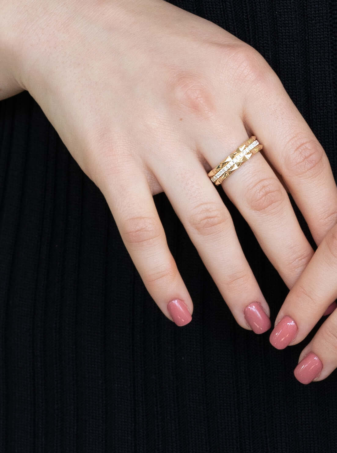 A hand with pink nails showcases two exquisite gold rings, the Diamond Pyramid Triple Row Ring featuring star patterns, elegantly resting against black textured fabric. Part of Janet Heller Fine Jewelry, these rings are available for preorder.