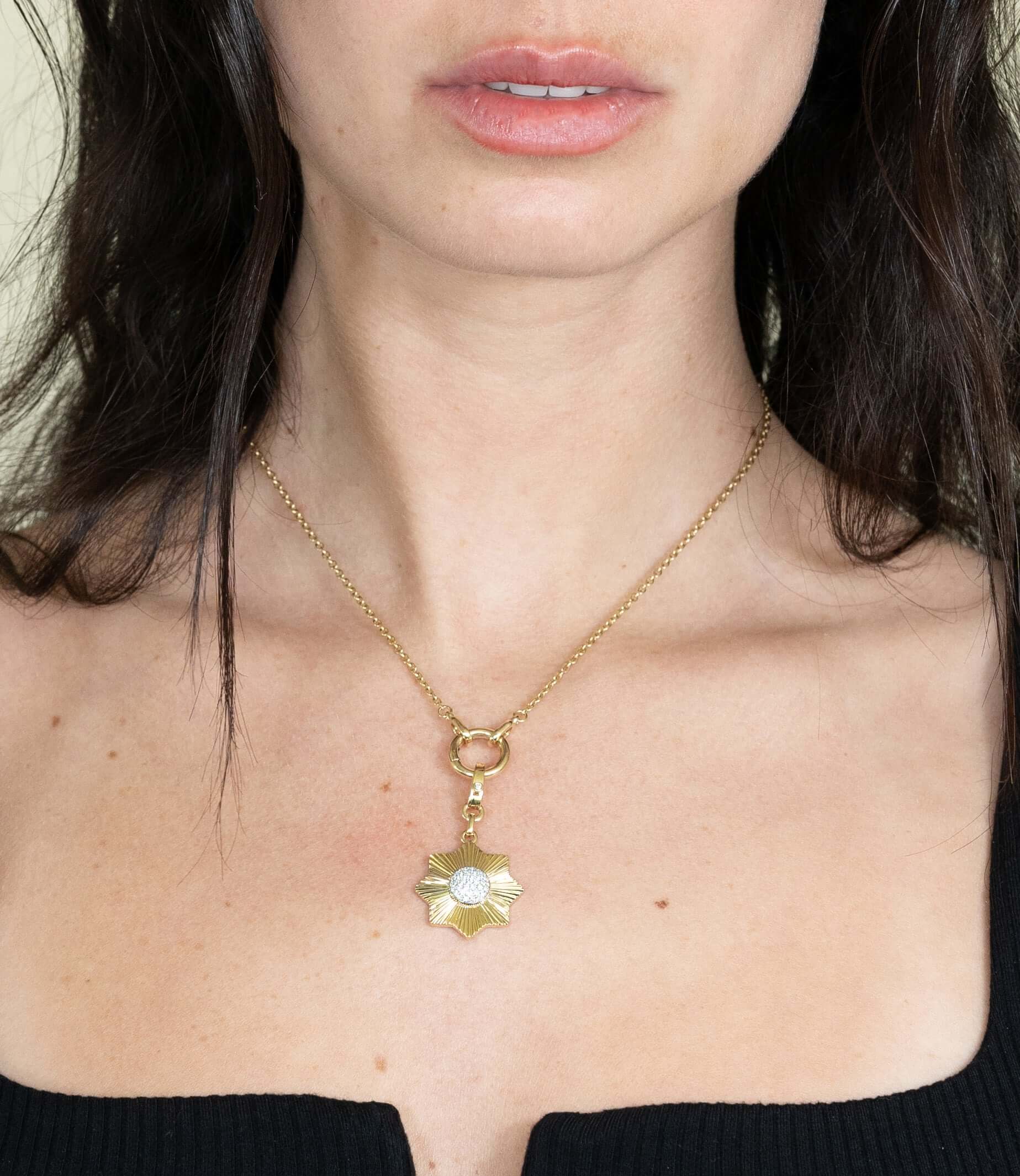 A woman wearing the Pave Diamond Sun Flower Charm necklace exudes elegance. Her long dark hair and black top highlight this fine jewelry piece against a plain background, while distinctive charms add personal customization to the exquisite accessory.
