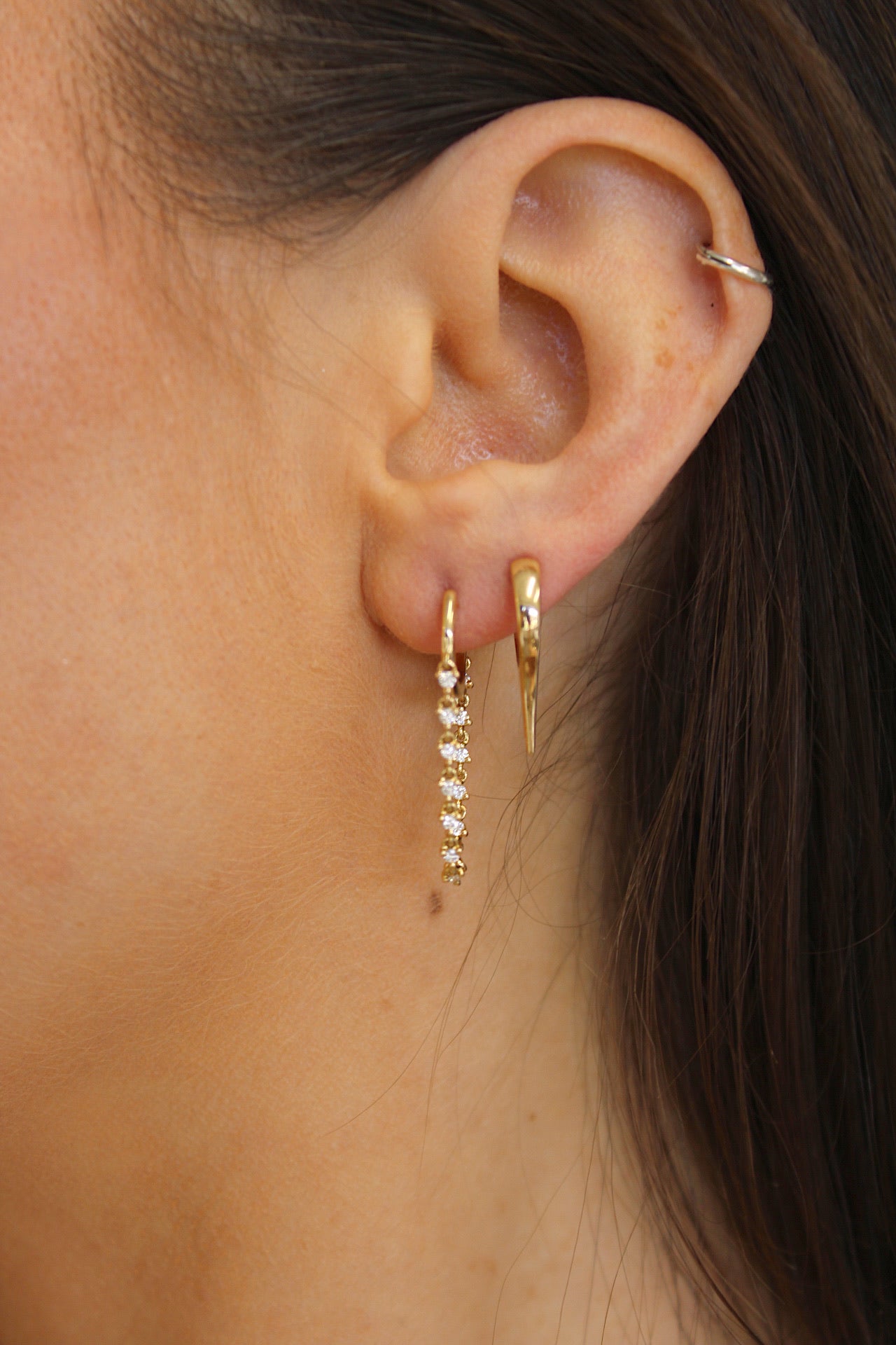 The Diamond Cascade Drop Huggies from Janet Heller Fine Jewelry are crafted in 14KT gold. The dangling hoop earrings feature evenly spaced round diamonds connected by a delicate chain. The earrings can be worn alone or layered along the ear with other earrings.