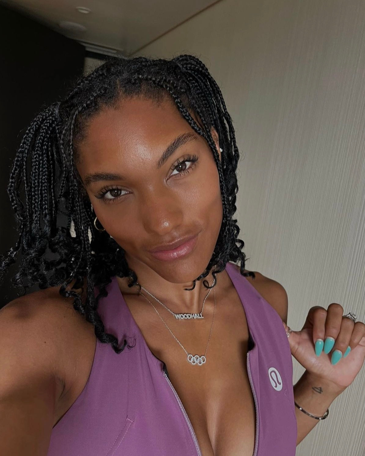 A woman with medium skin tone and braided hair smiles as she takes a selfie, wearing a purple sleeveless top, turquoise nails, and the Diamond Rings Necklace. The softly lit background hints at her excitement for its pre-order arrival.