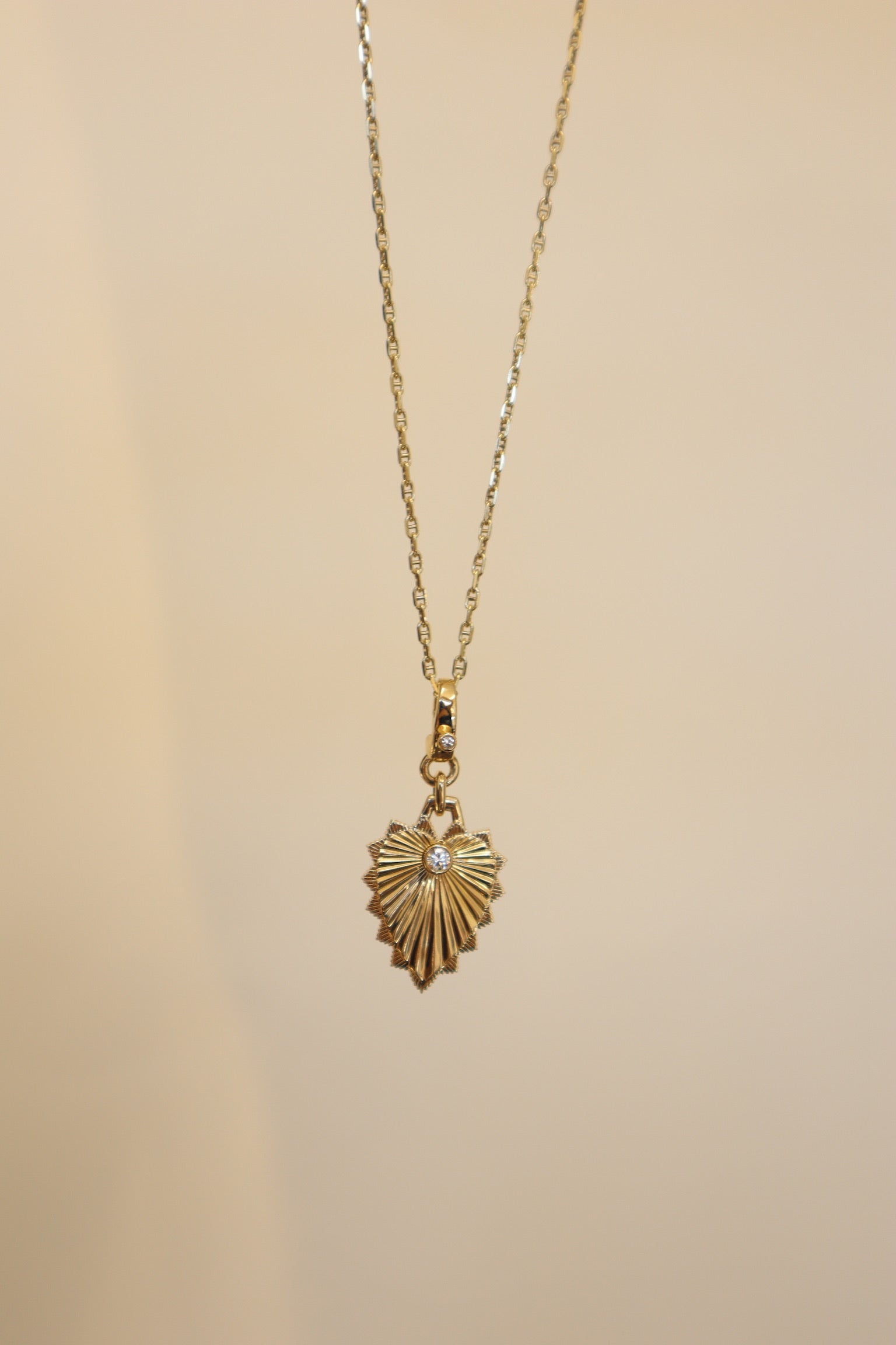 The Ribbed Diamond Heart Shield Charm from Janet Heller Fine Jewelry is crafted in 14KT yellow gold. It features a single round diamond on the shield with an additional round diamond on the bale. The clasp allows the charm to clip onto various chains and necklaces.