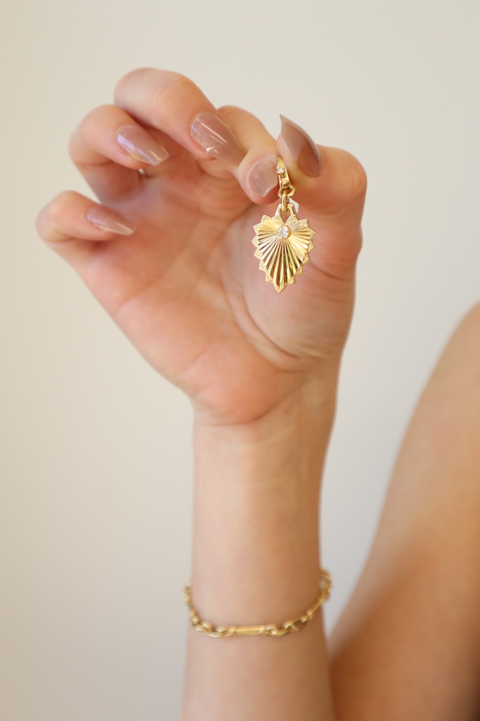 The Ribbed Diamond Heart Shield Charm from Janet Heller Fine Jewelry is crafted in 14KT yellow gold. It features a single round diamond on the shield with an additional round diamond on the bale. The clasp allows the charm to clip onto various chains and necklaces.