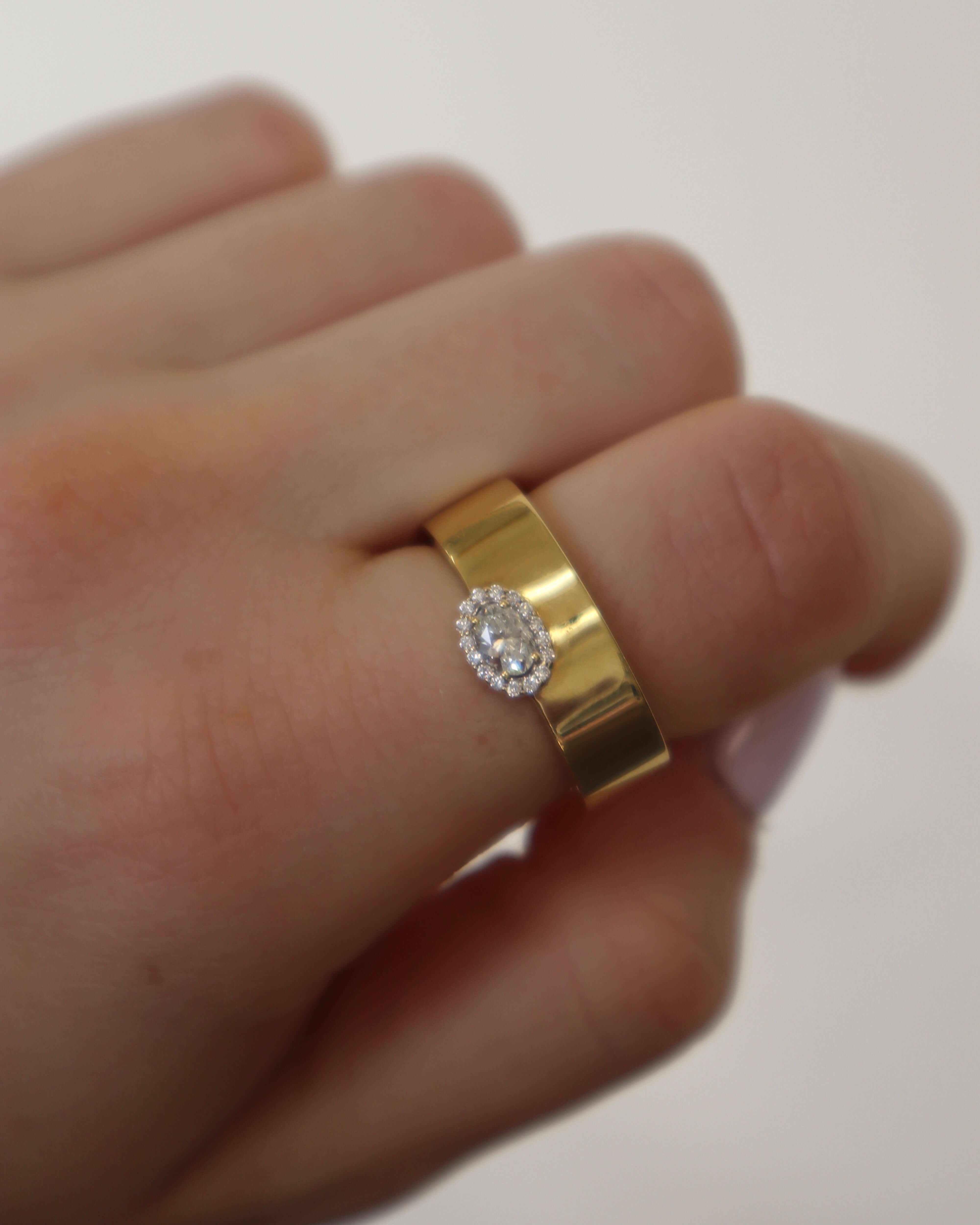The Diamond Oval Cut Ring from Janet Heller Fine Jewelry is crafted in 18KT gold. The ring features an oval diamond surrounded by several smaller diamonds.