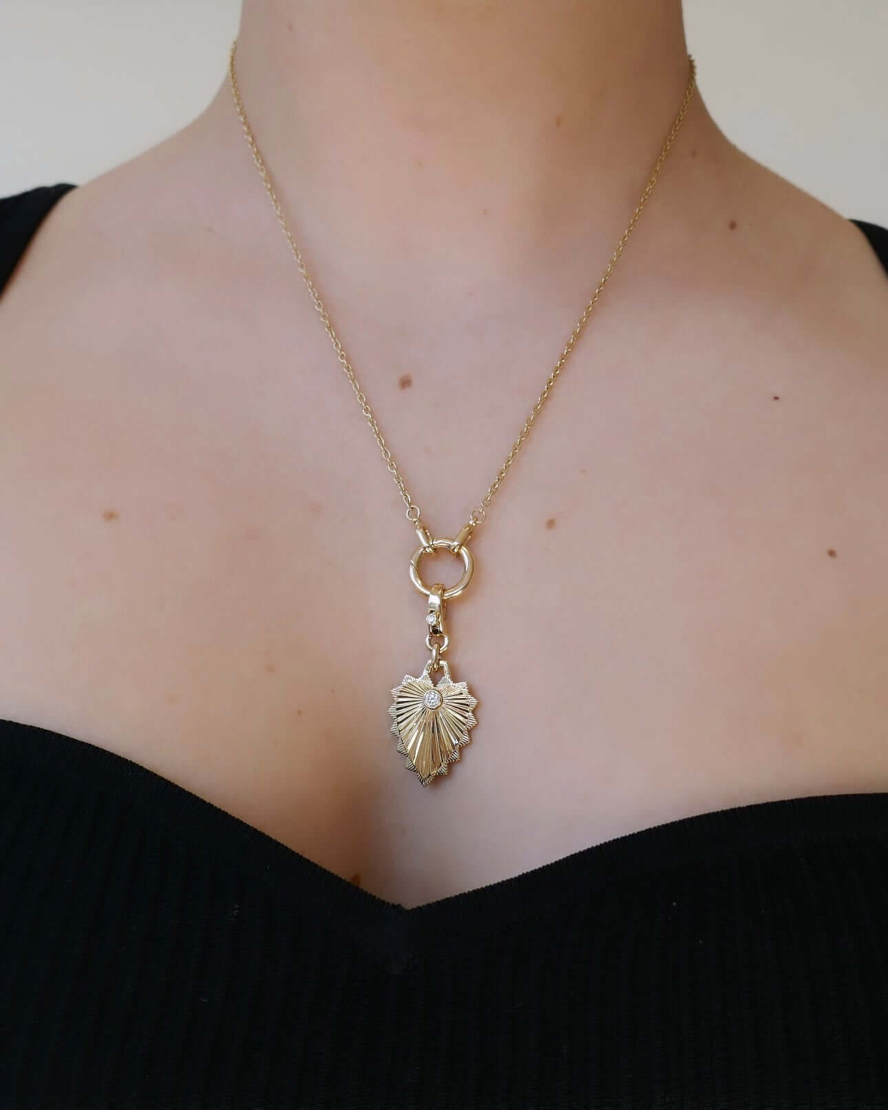 The Ribbed Diamond Heart Shield Charm necklace from Janet Heller Fine Jewelry features a ribbed design with scalloped edges and a diamond in the center of the pendant. The diamond clasp clips easily onto various Janet Heller Fine Jewelry chains and necklaces.