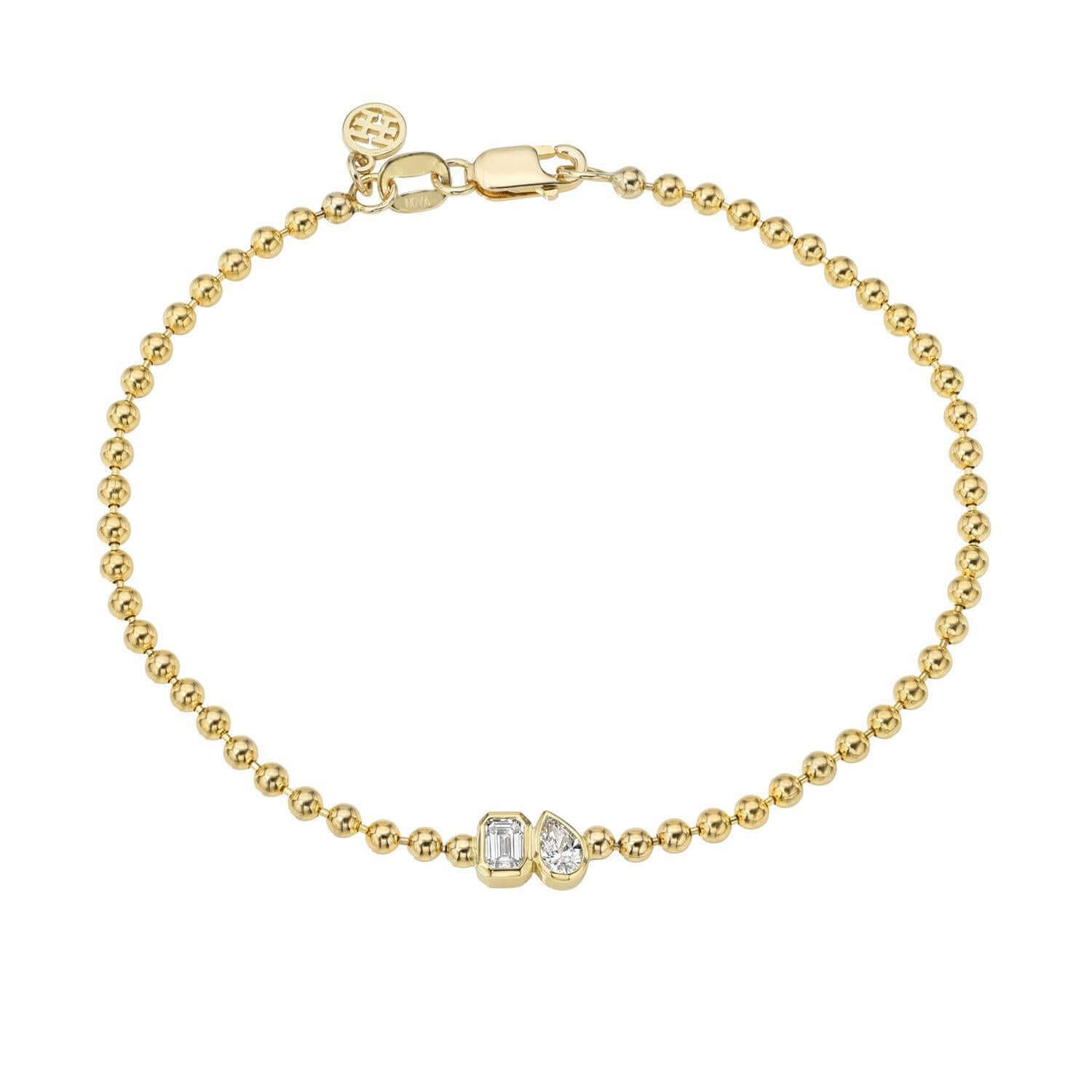 The Emerald & Pear Toi Et Moi Bracelet is a delicate gold beaded bracelet featuring two small geometric-shaped clear stones at the center. It elegantly symbolizes love and partnerships with its secure clasp and a round charm engraved near the closure, echoing Toi et Moi designs.