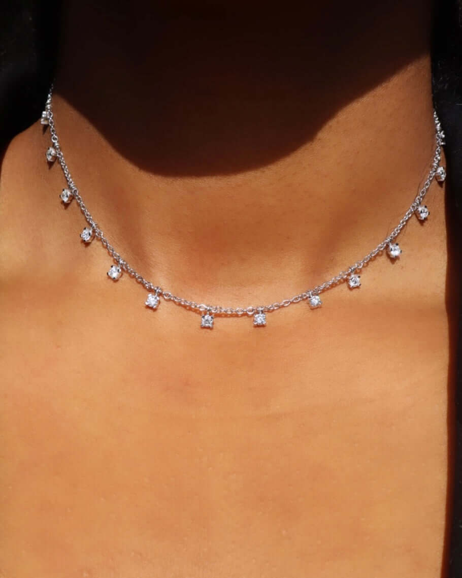 A close-up shows a persons neck adorned with the Diamond Hallie Necklace by Janet Heller Fine Jewelry, featuring evenly spaced sparkling pendants on silver. The softly blurred background highlights the necklaces intricate design and bespoke customizations.