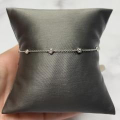 A delicate Bezel Diamond Station Bracelet with small, evenly spaced diamonds displayed on a black cushion, held by a hand—an exquisite example of custom jewelry from Janet Heller Fine Jewelry.