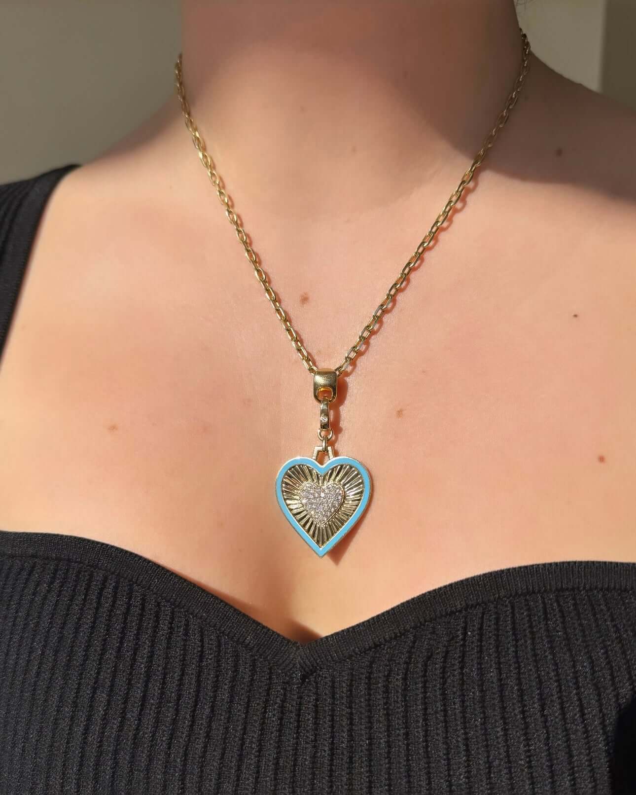 The Diamond Blue Enamel Heart Charm from Janet Heller Fine Jewelry is crafted in 14KT gold and features a blue-bordered gold and diamond heart pendant with a diamond clasp. The charm clips directly onto various Janet Heller Fine Jewelry chains and necklaces.