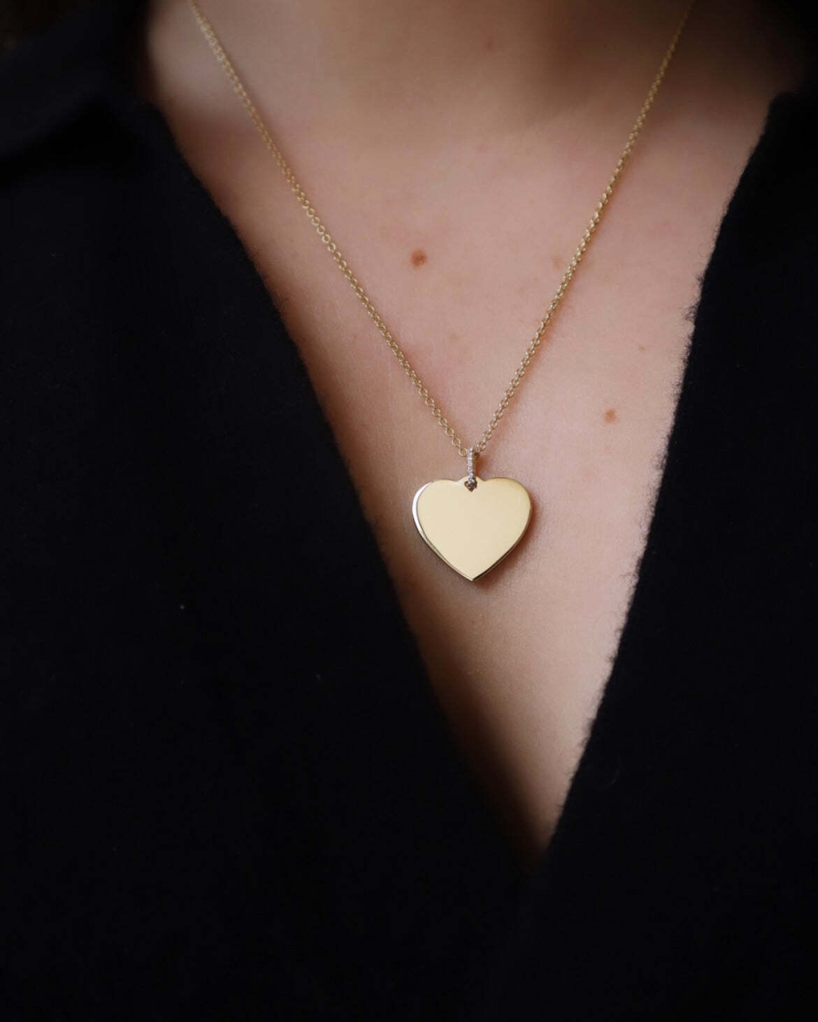 A close-up of a person wearing the Large Heart Engravable Pendant Necklace—this personalized piece rests elegantly against a dark, partially open shirt.