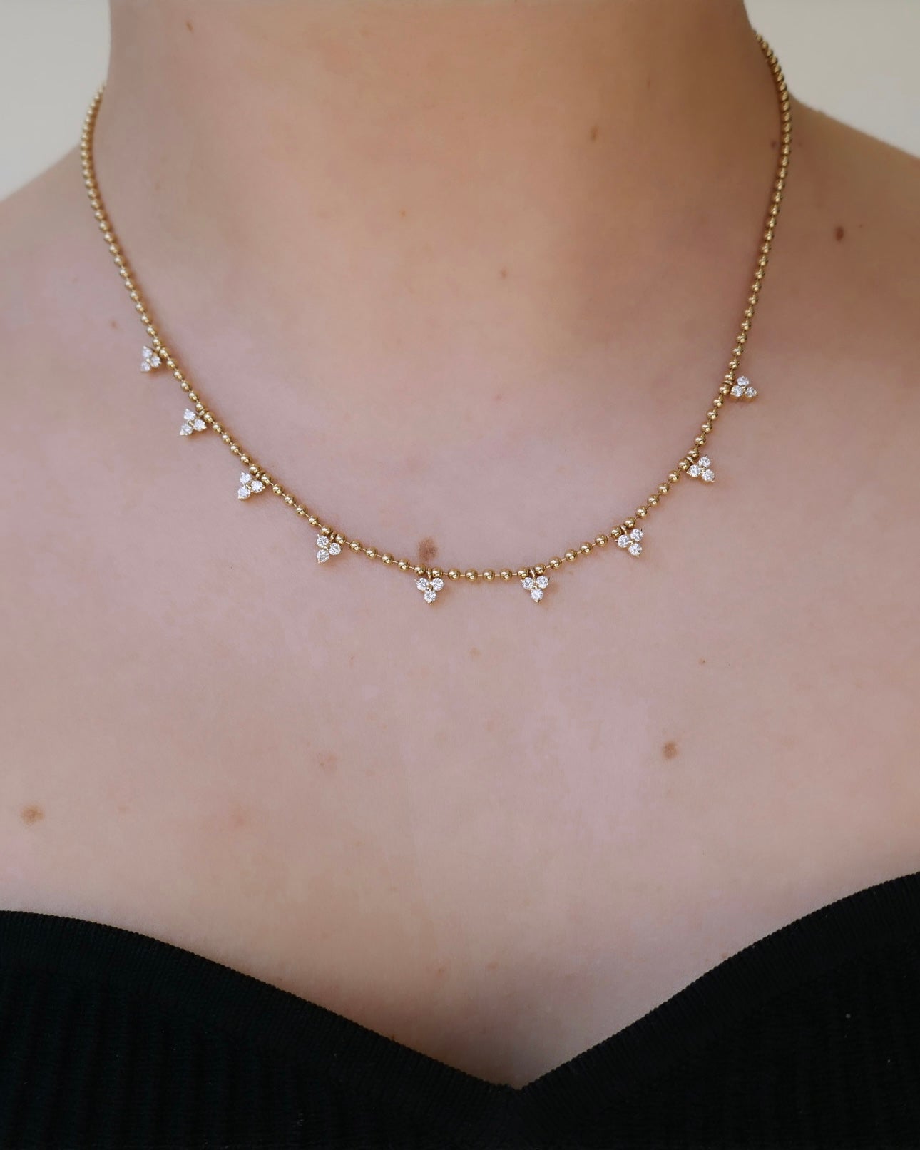Enhance your neckline with the Beaded Diamond Cluster Necklace by Janet Heller Fine Jewelry. This gold-toned piece boasts signature triangular crystal clusters, beautifully complementing a dark off-the-shoulder top. Contact us for personalized customizations to match your style.
