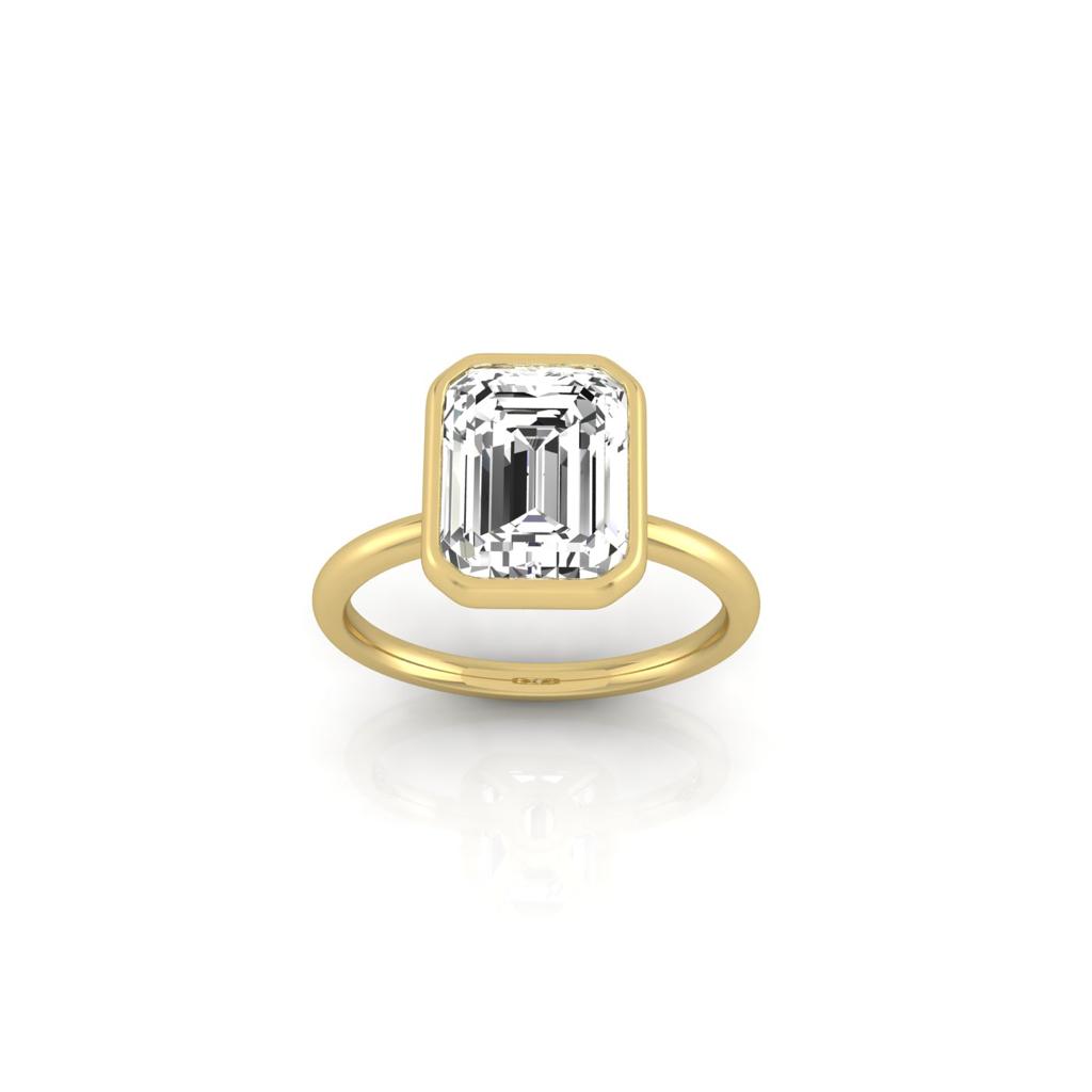 Introducing the Classic Bezel: an 18KT gold ring showcasing a bezel-set diamond with a large rectangular emerald cut, elegantly displayed against a plain white background.