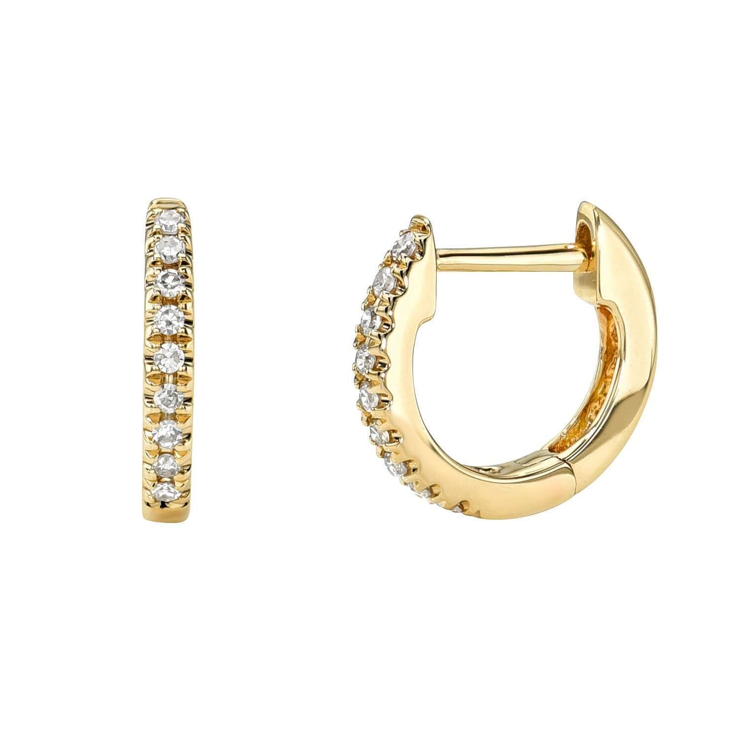The Mini Diamond Anika Huggies by Janet Heller Fine Jewelry are small gold hoops, each featuring a row of sparkling white diamonds. One earring is shown from the side, the other from the front, highlighting both clasp and design.