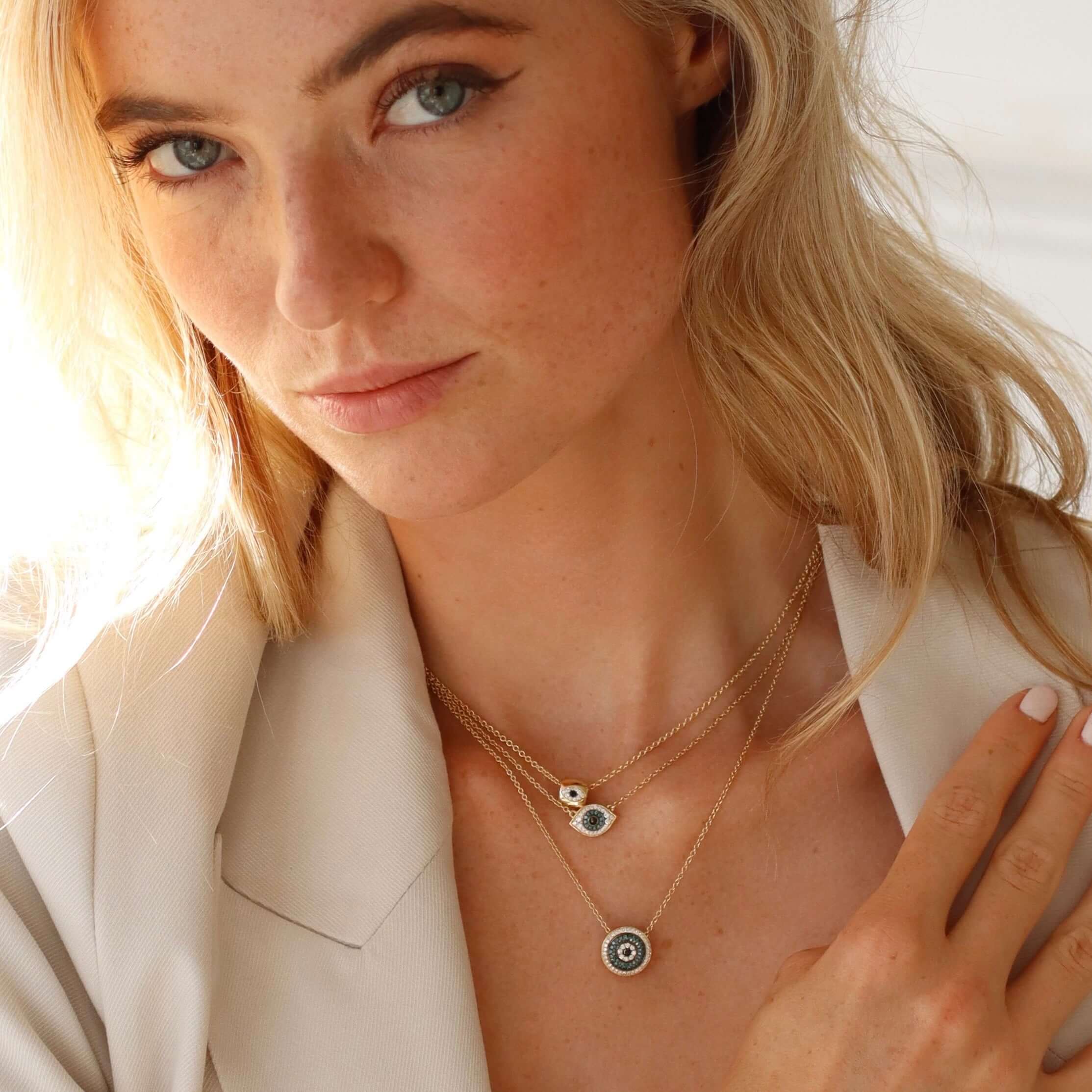 The Mini Round Blue Diamond Evil Eye Charm from Janet Heller Fine Jewelry is crafted in 14KT gold and features multi-colored diamonds in white and blue with a black center diamond. The diamond clasp clips easily onto various Janet Heller Fine Jewelry chains and necklaces.