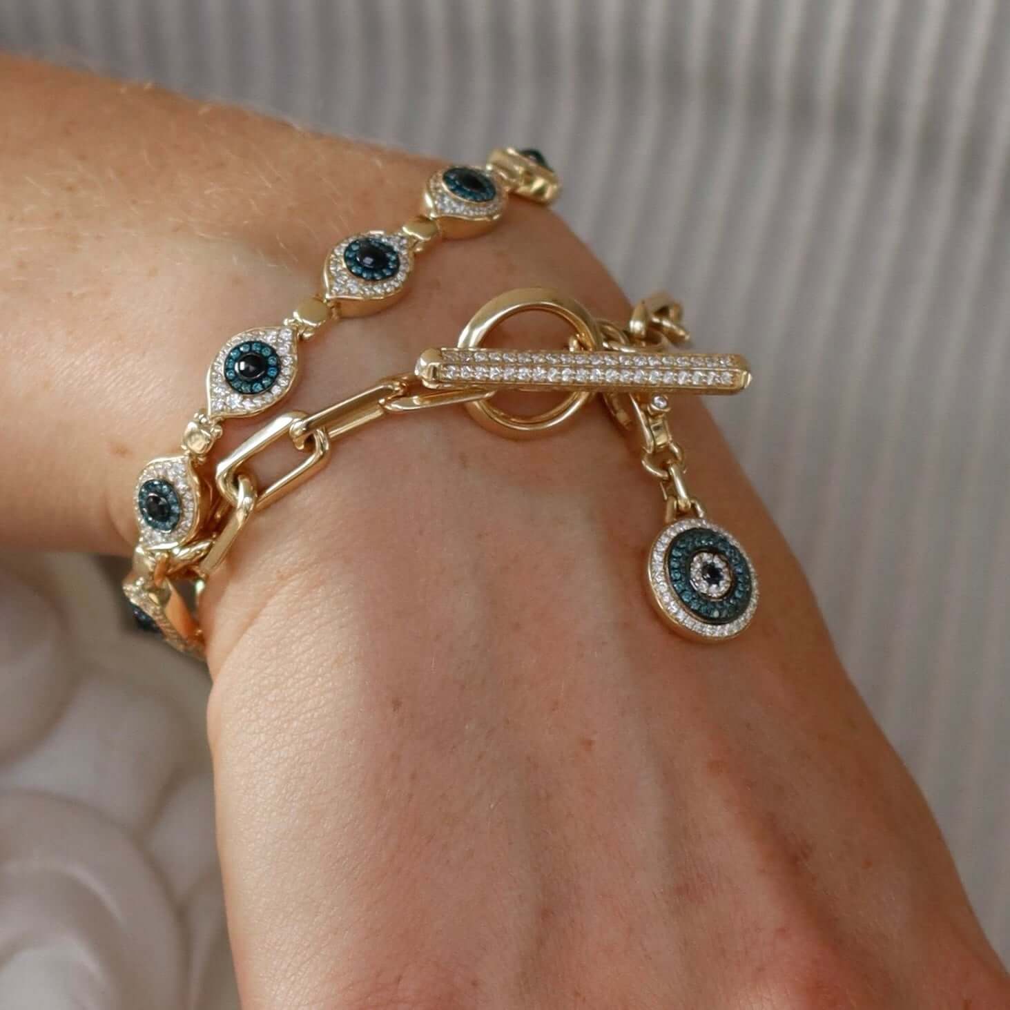 The Mini Round Blue Diamond Evil Eye Charm from Janet Heller Fine Jewelry is crafted in 14KT gold and features an eye-shaped charm with blue and white diamonds. The diamond clasp clips directly onto various Janet Heller Fine Jewelry chains and necklaces.