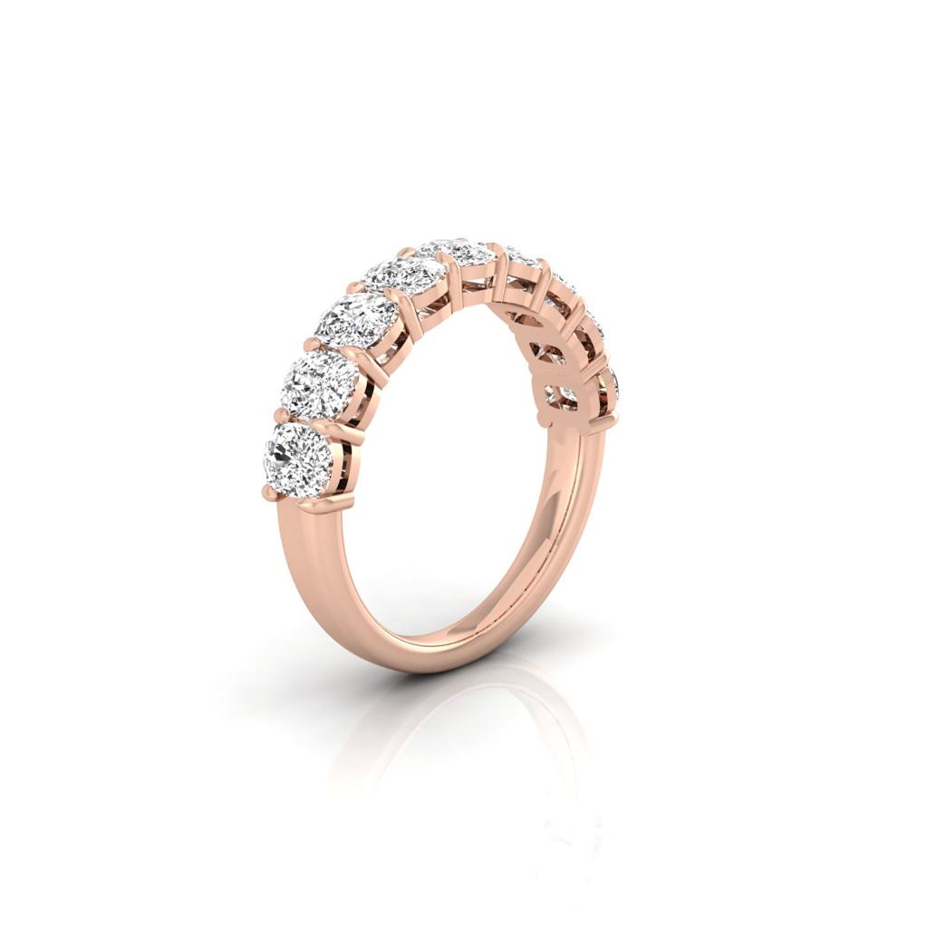 The Half Diamond Eternity Ring, crafted in 18KT rose gold, showcases a row of seven sparkling round-cut diamonds with VS Clarity. Its elegantly curved band has a polished finish that beautifully reflects light against a white, minimalistic background.