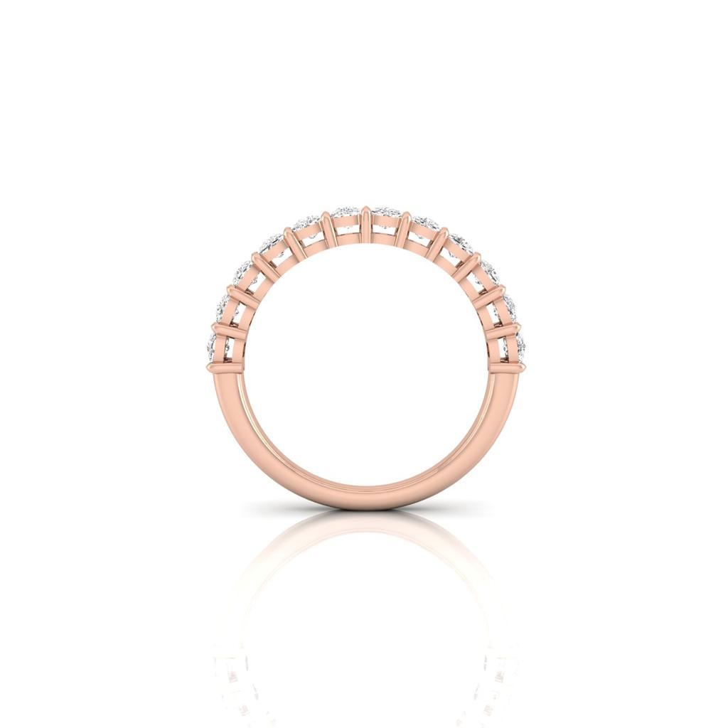 A side view of the Half Diamond Eternity Ring shows it crafted in 18KT rose gold with a row of small, round, white diamonds, featuring VS Clarity. It rests on a reflective white surface, highlighting its elegant and minimalist design.