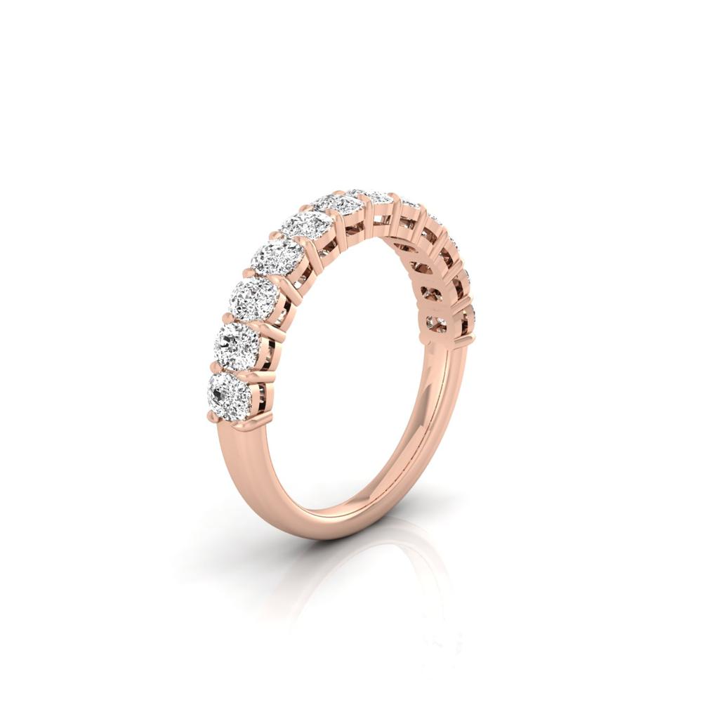 The Half Diamond Eternity Ring, crafted in 18KT rose gold, showcases a row of VS Clarity diamonds on its band. Its elegant design enhances the brilliance of the stones against a reflective white surface.