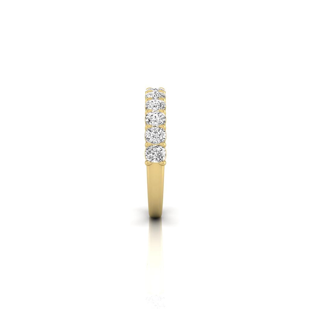The Half Diamond Eternity Ring, crafted in 18KT gold, features a row of seven small, round, sparkling diamonds with exceptional VS clarity. Its sleek and elegant design is showcased against a white background.