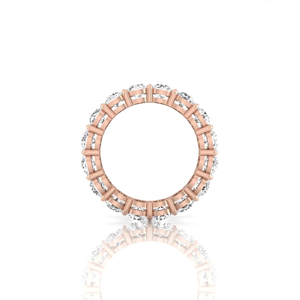 The Full Lab Grown Diamond Eternity Ring, crafted from 18KT rose gold, showcases F color VS clarity stones in a halo design encircling the band. The diamonds are evenly spaced on a white reflective surface, creating a stunning and elegant sparkling appearance.