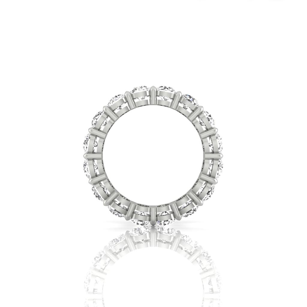 The Full Lab Grown Diamond Eternity Ring in silver showcases a circle of evenly spaced, round-cut clear gemstones with F Color VS Clarity. Reflected on a glossy white surface, each stones sparkle and perfect symmetry enhance its stunning appearance.