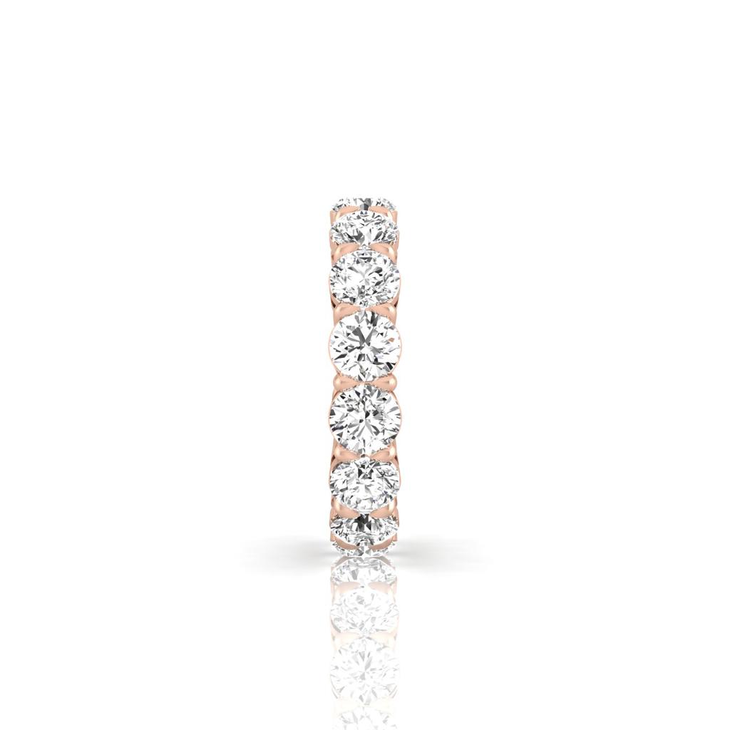 The Full Lab Grown Diamond Eternity Ring, crafted in 18KT rose gold, features a seamless row of round diamonds in a sleek design. Its elegance shines as it reflects soft light on a smooth white surface.