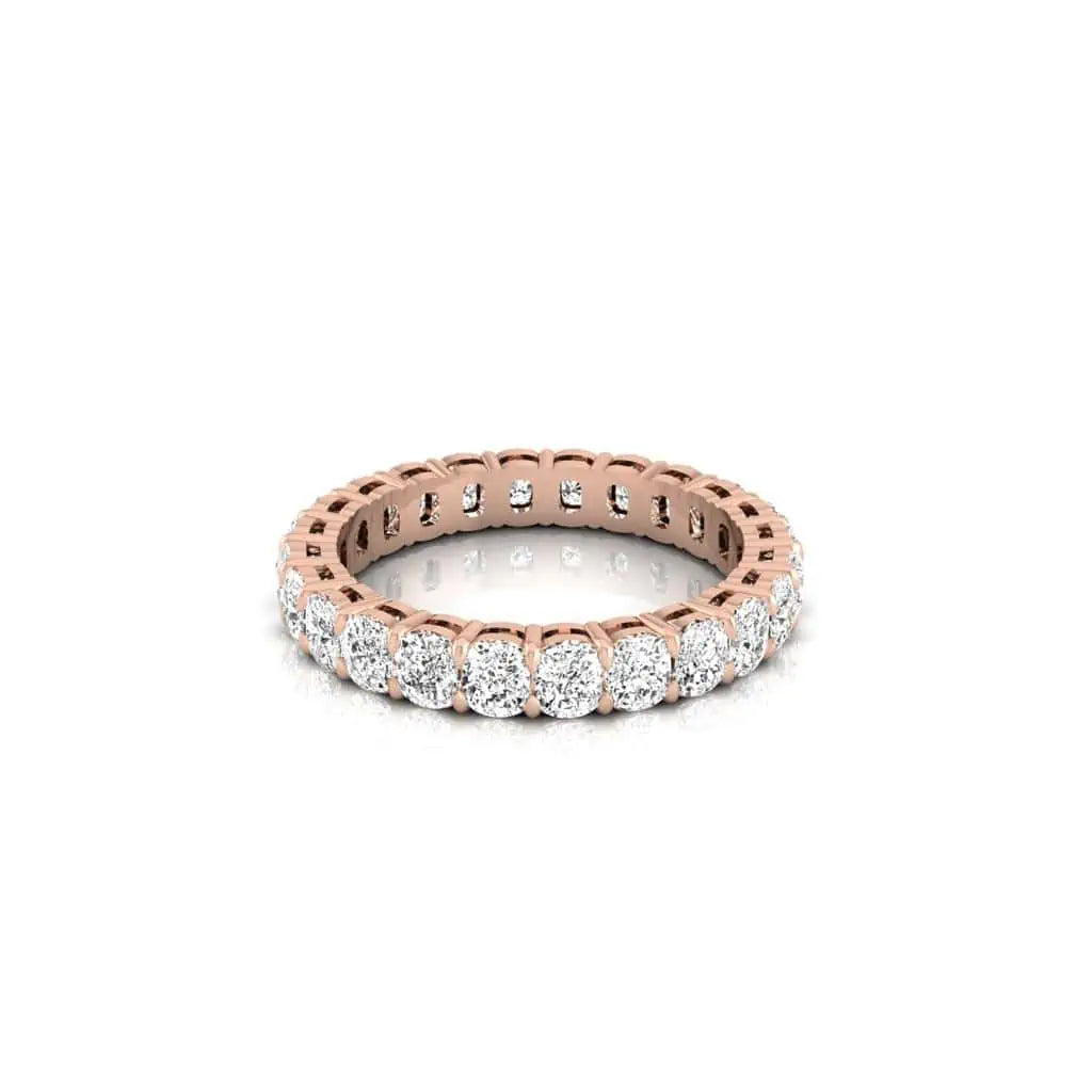 The Full Diamond Eternity Ring, made from 18KT rose gold, features a continuous row of round, sparkling diamonds set around the band. It rests on a glossy white surface to enhance its elegant design and custom carat weights.