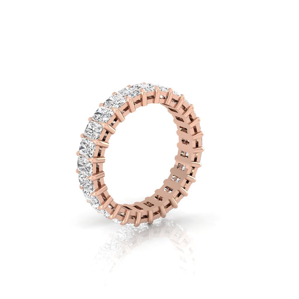 The Full Lab Grown Diamond Eternity Ring is an 18KT rose gold band adorned with sparkling diamonds encircling it. Displayed upright on a white reflective surface, it showcases the intricate design and F Color VS Clarity brilliance of its diamonds.