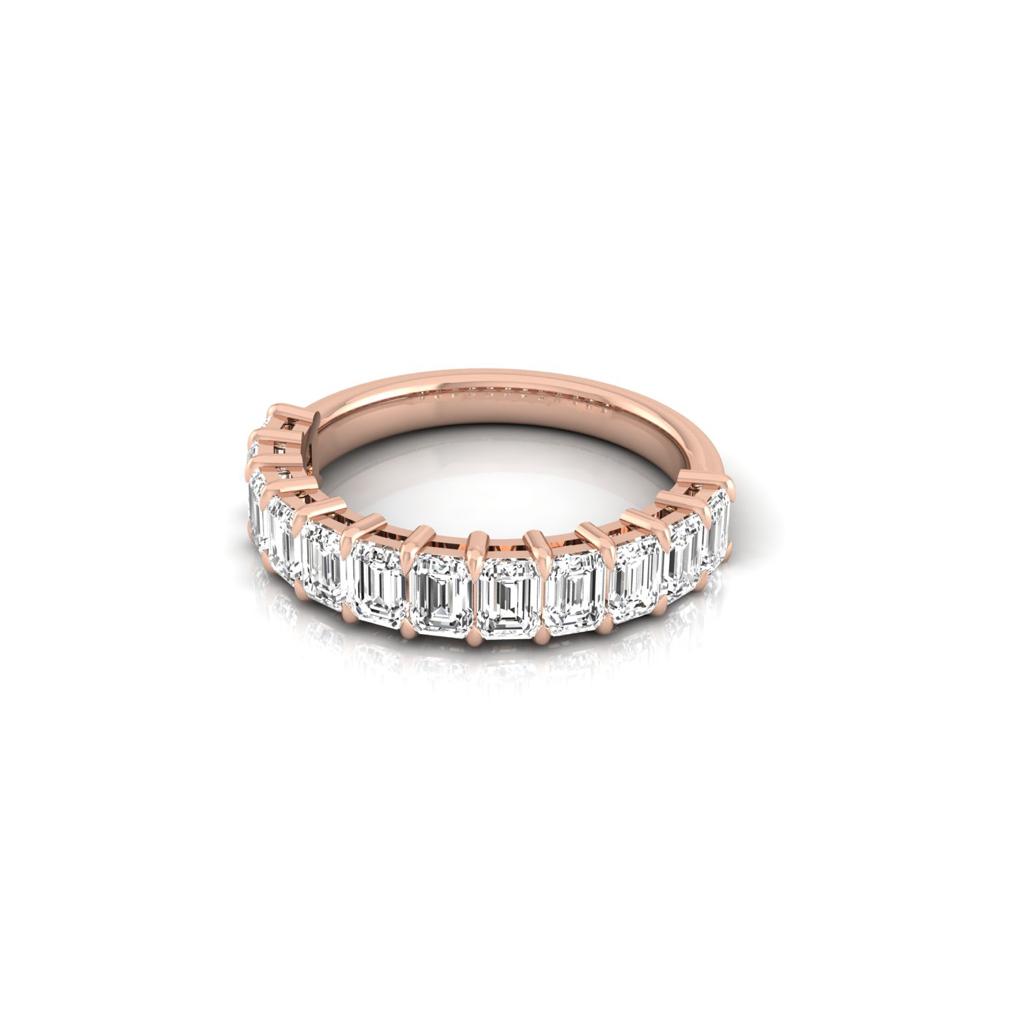 The Half Diamond Eternity Ring, crafted from 18KT rose gold, showcases emerald-cut diamonds with VS clarity set elegantly along the top half, beautifully displayed against a white background.