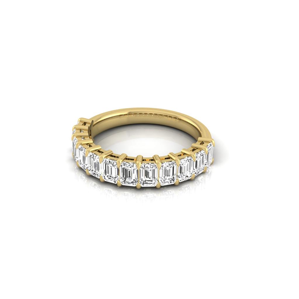 The Half Diamond Eternity Ring, a stunning 18KT gold piece, features a row of rectangular-cut clear gemstones and diamonds arranged in a prong setting with VS clarity. Displayed on a reflective white surface, its elegant design shines.