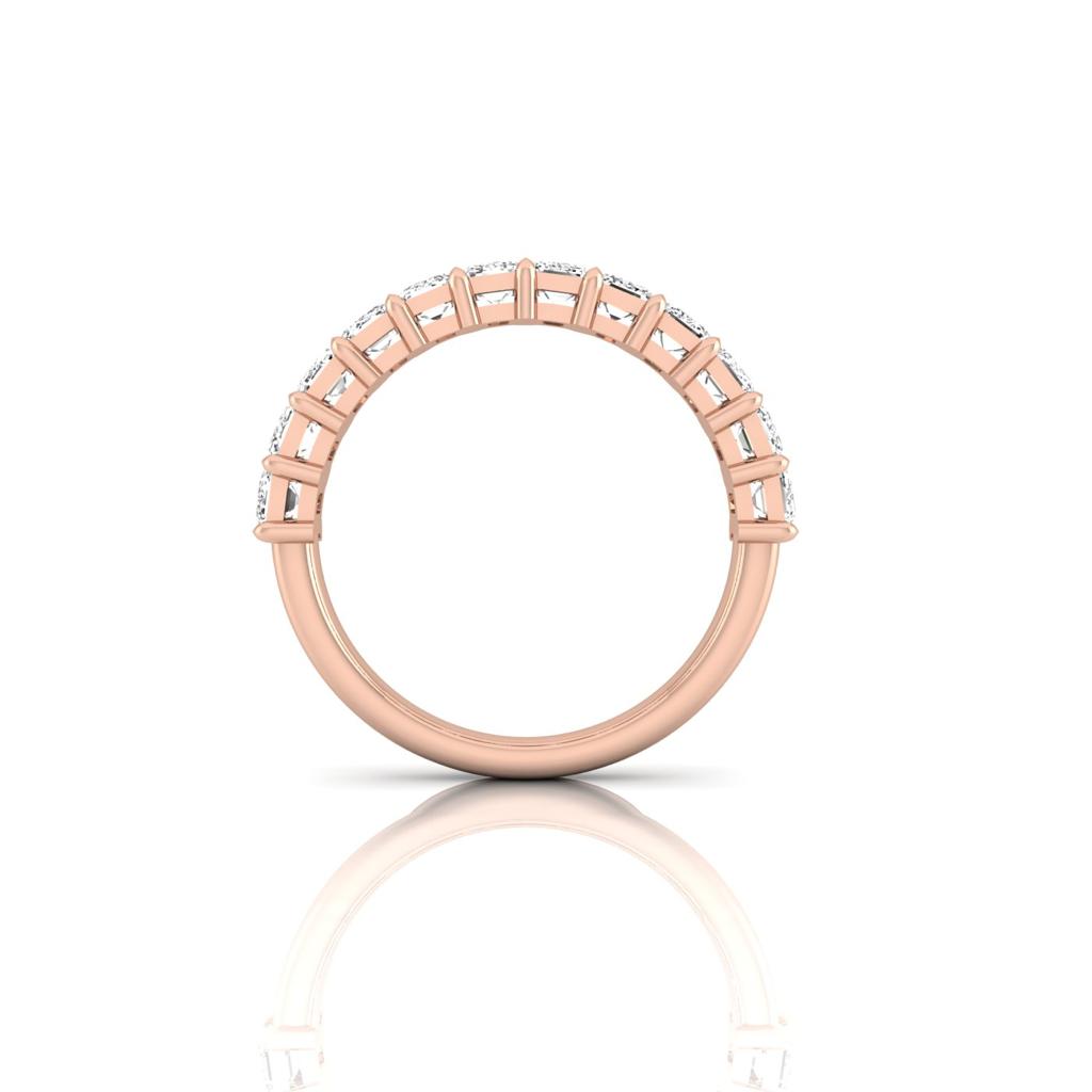 The Half Diamond Eternity Ring features VS clarity diamonds set along the top half of an 18KT rose gold band, offering a radiant sparkle. The elegant prong setting and polished finish are beautifully highlighted when viewed from the side, all reflected on a white surface.