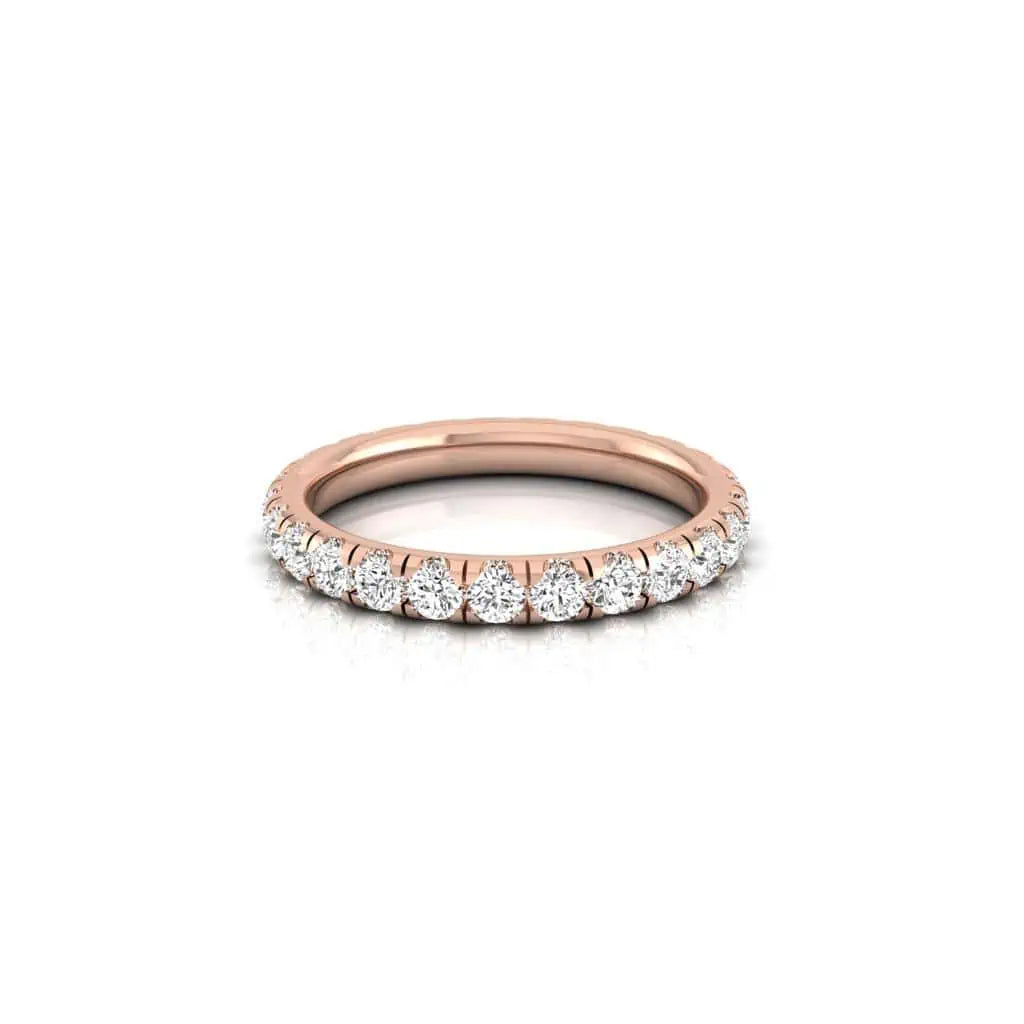 The 1ct Round Diamond Eternity Ring features a rose gold band made from 18KT gold, embellished with VS clarity diamonds along the top half. When placed on a reflective surface, it elegantly displays its stunning design.