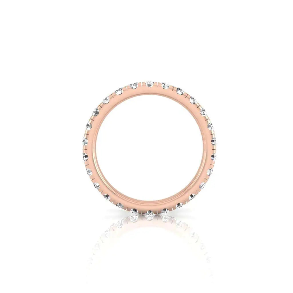 The 1ct Round Diamond Eternity Ring, crafted from 18KT rose gold and featuring lab-created VS clarity diamonds around the band, is showcased against a white background with a subtle reflection beneath.