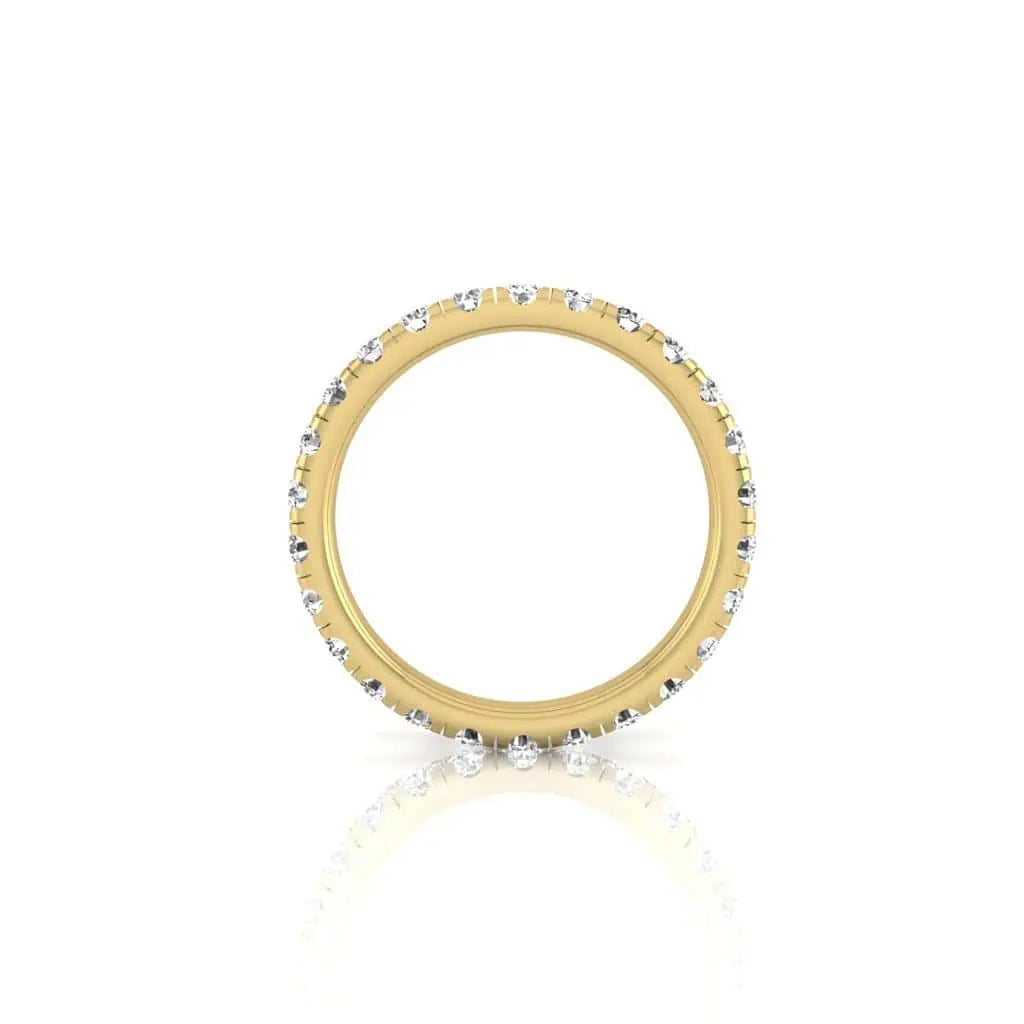 The 1ct Round Diamond Eternity Ring, crafted from 18KT gold, displays small VS clarity diamonds around its band. It stands upright on a plain white background, highlighting its full circular profile with delicate reflections below.