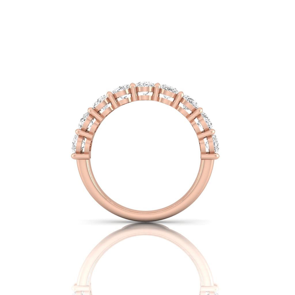 The Half Diamond Eternity Ring is a rose gold piece made from 18KT gold, featuring a row of small, sparkling diamonds with VS Clarity along the top half. It’s displayed upright and reflected on a glossy white background.