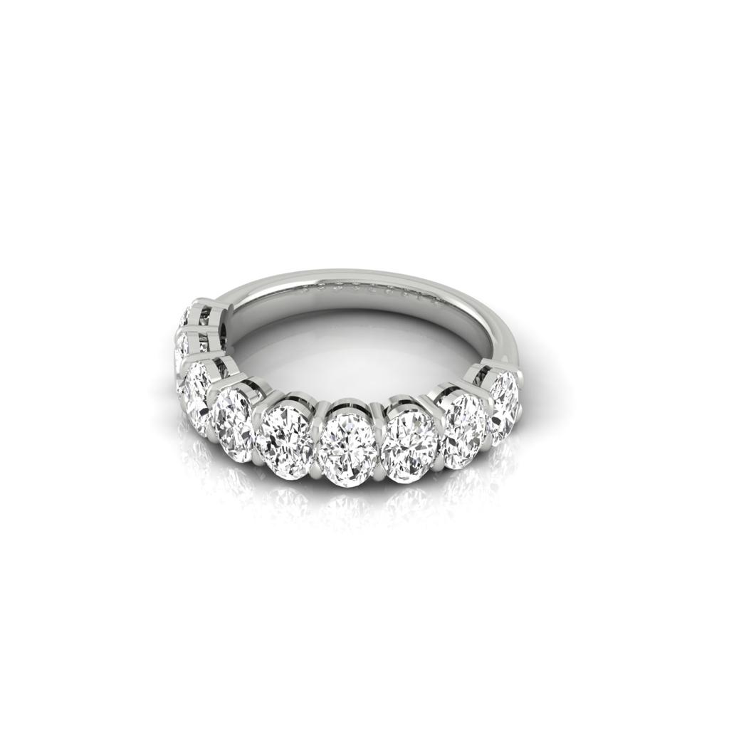 The Half Diamond Eternity Ring, crafted from silver and featuring a row of VS Clarity diamonds along the top half, is elegantly displayed on a reflective white surface, showcasing its bright and clear gemstones.