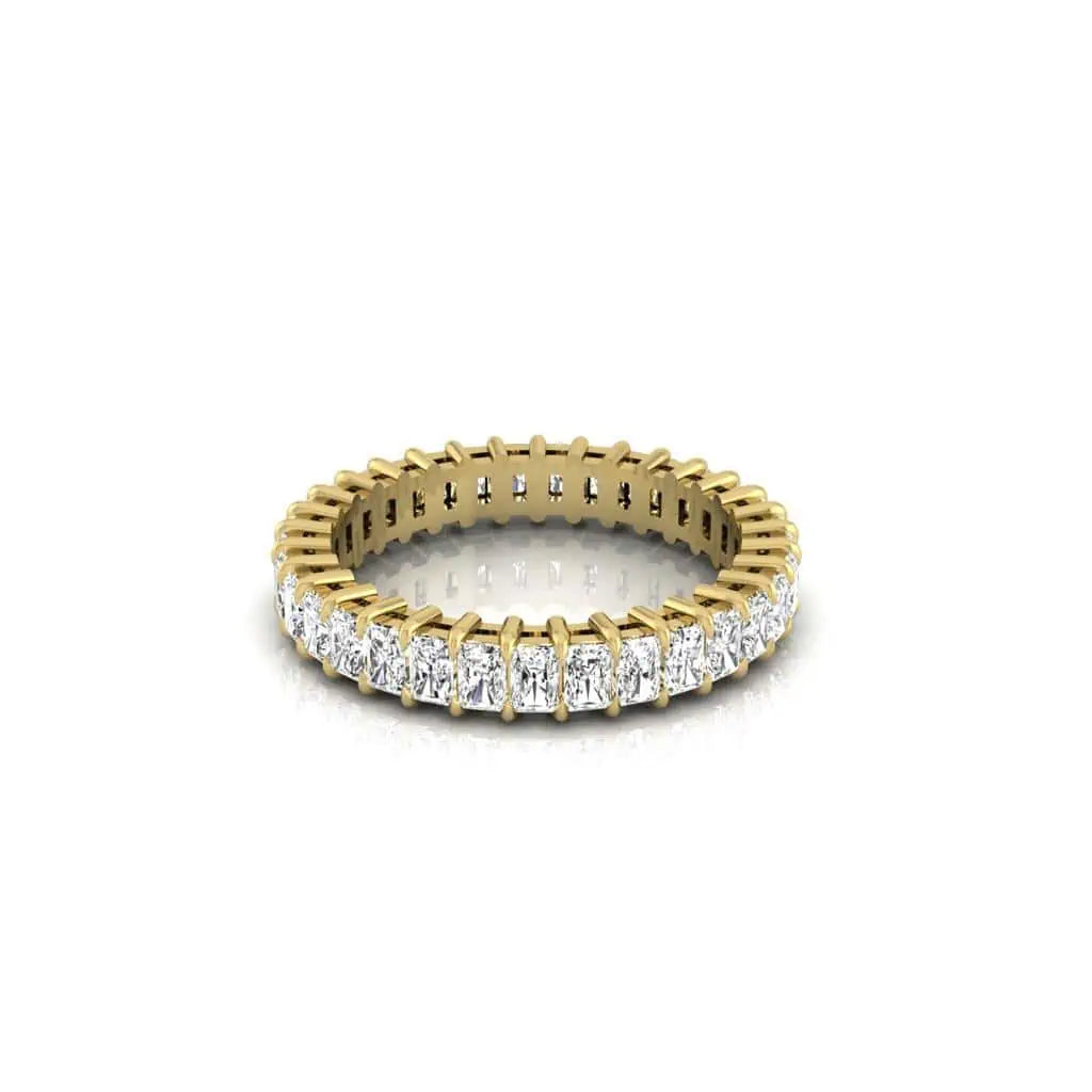 The Full Diamond Eternity Ring, crafted from 18KT gold, features a continuous band of F Color round-cut diamonds with VS Clarity. Displayed on a reflective white surface, its intricate design and brilliance are highlighted.