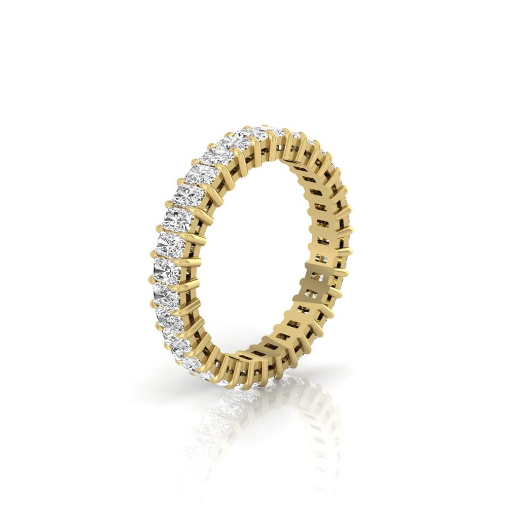 The Full Lab Grown Diamond Eternity Ring, crafted in 18KT gold, features F Color VS Clarity round diamonds in a prong setting. Positioned upright, it dazzles on a reflective surface below.