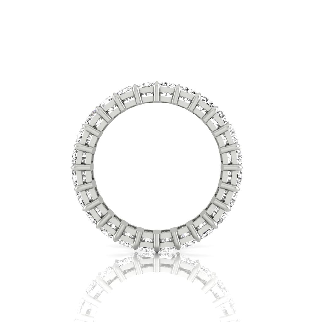 The Full Lab Grown Diamond Eternity Ring is an 18KT gold ring with a circular design, featuring small diamond-like stones set around its entire circumference. It showcases F Color VS Clarity and is displayed upright with its reflection visible on the white background.
