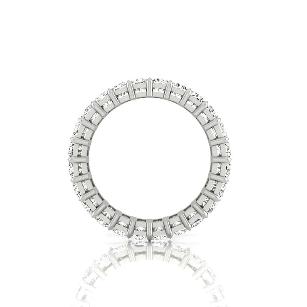 The Full Diamond Eternity Ring, circular and silver, showcases small VS Clarity diamonds embedded around the band. It is elegantly reflected on a glossy white surface, enhancing its symmetry and brilliance.