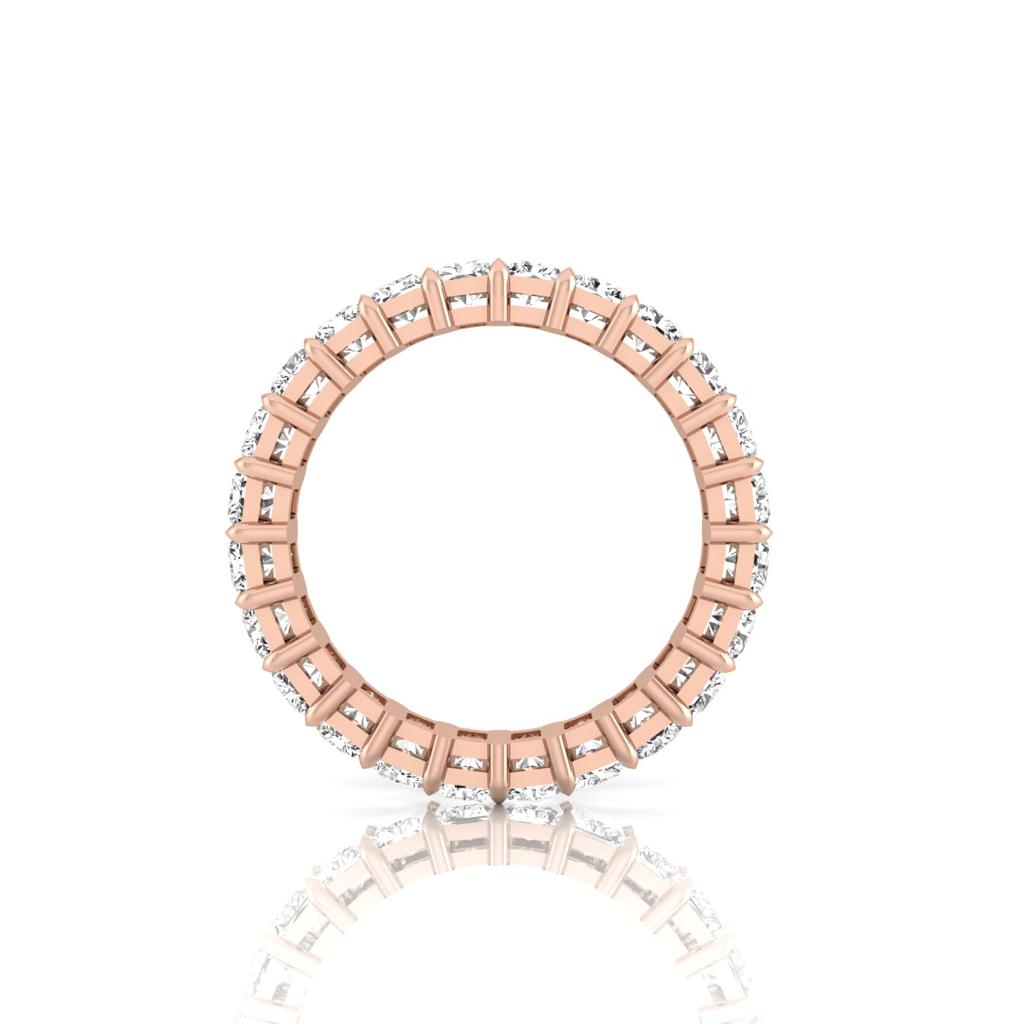 The Full Lab Grown Diamond Eternity Ring, crafted from 18KT rose gold, showcases a continuous circle of small diamonds (F color, VS clarity) around the band. Displayed upright on a reflective surface, its intricate design and symmetry are highlighted by soft lighting.